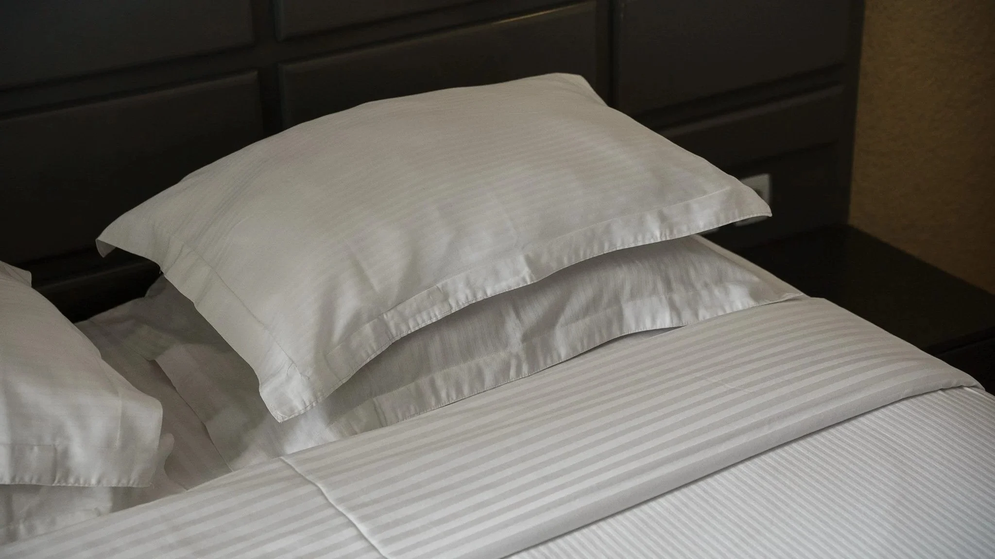 Neatly made hotel bed at Quality INN Hotel Kigali, Rwanda with crisp white pillows, striped bedding, dark headboard, and side table.
