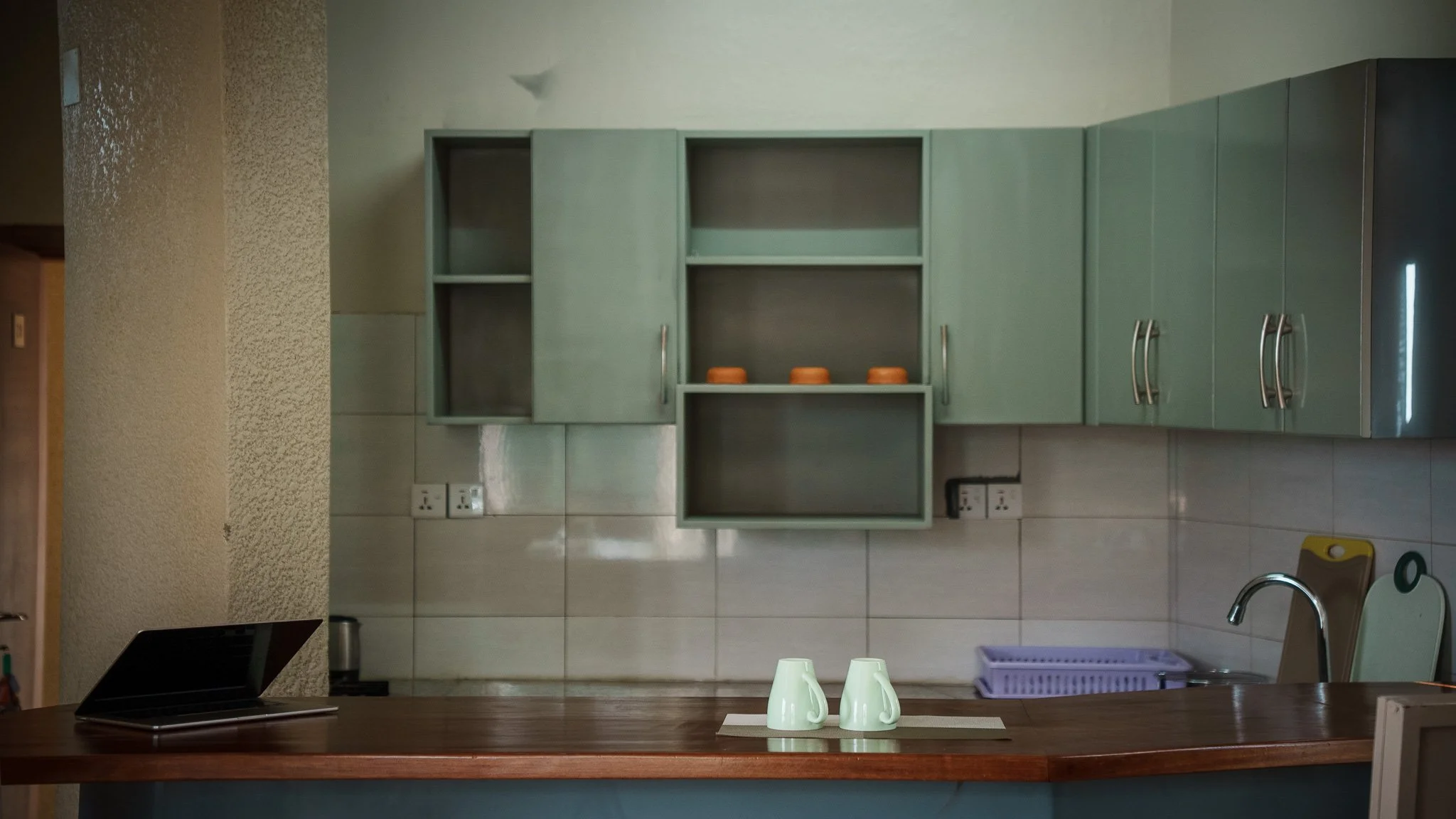Modern kitchenette at Quality Inn Hotel Kigali, Rwanda, featuring cabinets, a wooden counter with two mugs, and a tidy sink—ideal for international travelers seeking a home-away-from-home experience.
