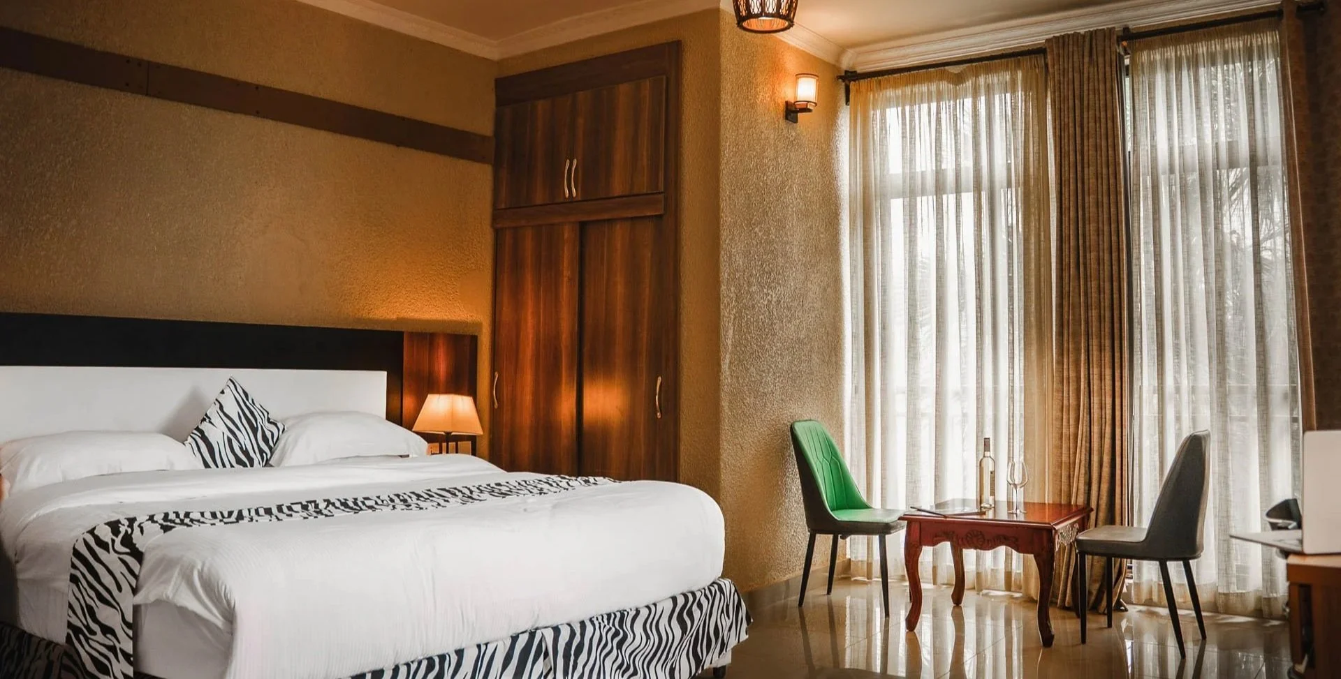 Quiet and comfortable hotel room with white bedding, zebra print accent, seating area, and large windows, offering a relaxing stay at Quality Inn Hotel Kigali, Rwanda.