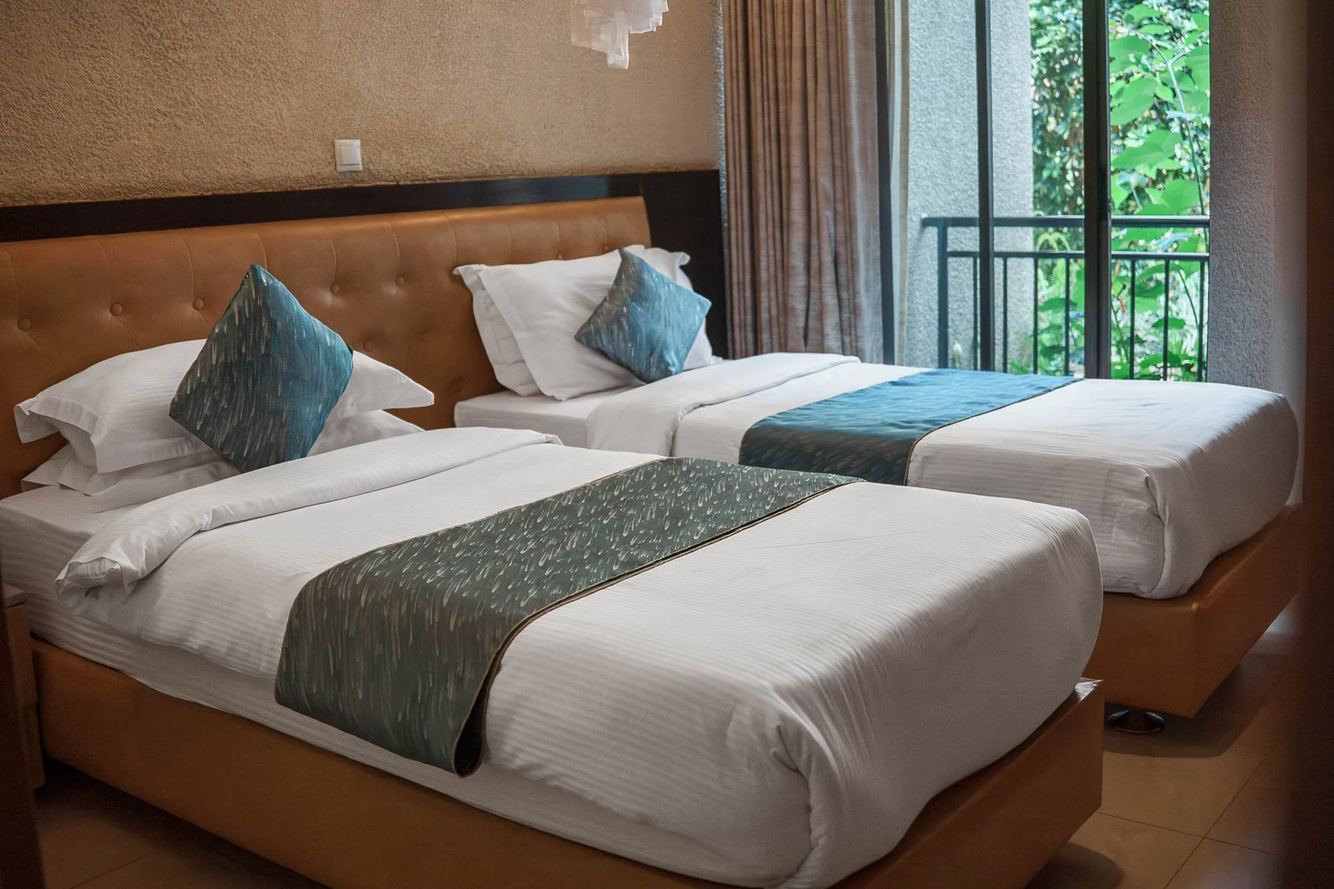 Twin bedroom at Quality INN Hotel Kigali, Rwanda with white linens, blue and green bed runners, and balcony overlooking greenery.
