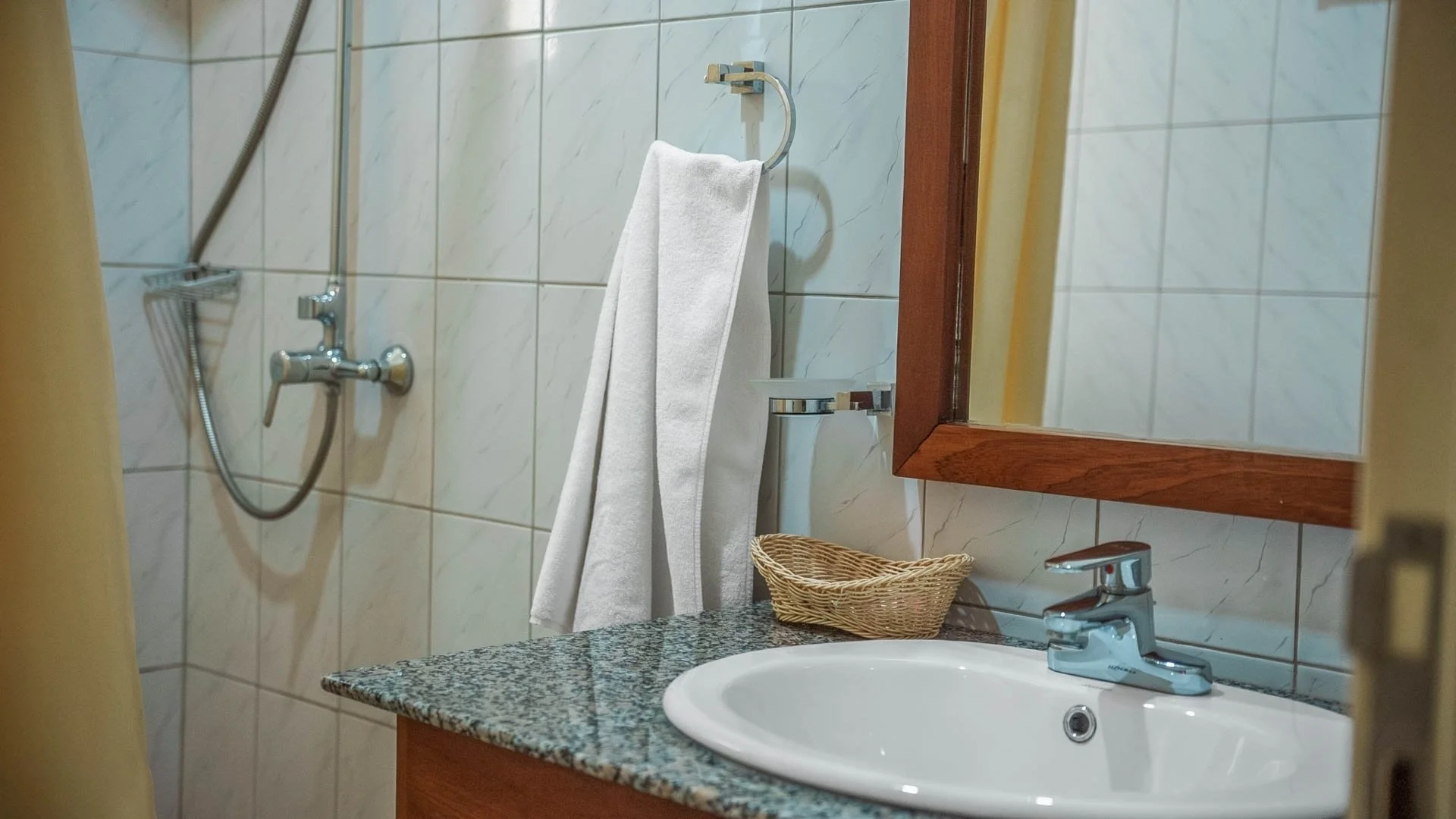 Bathroom with a sink, mirror, soap dish, towel, shower area and tiled wall at Quality Inn Hotel Kigali, Rwanda.