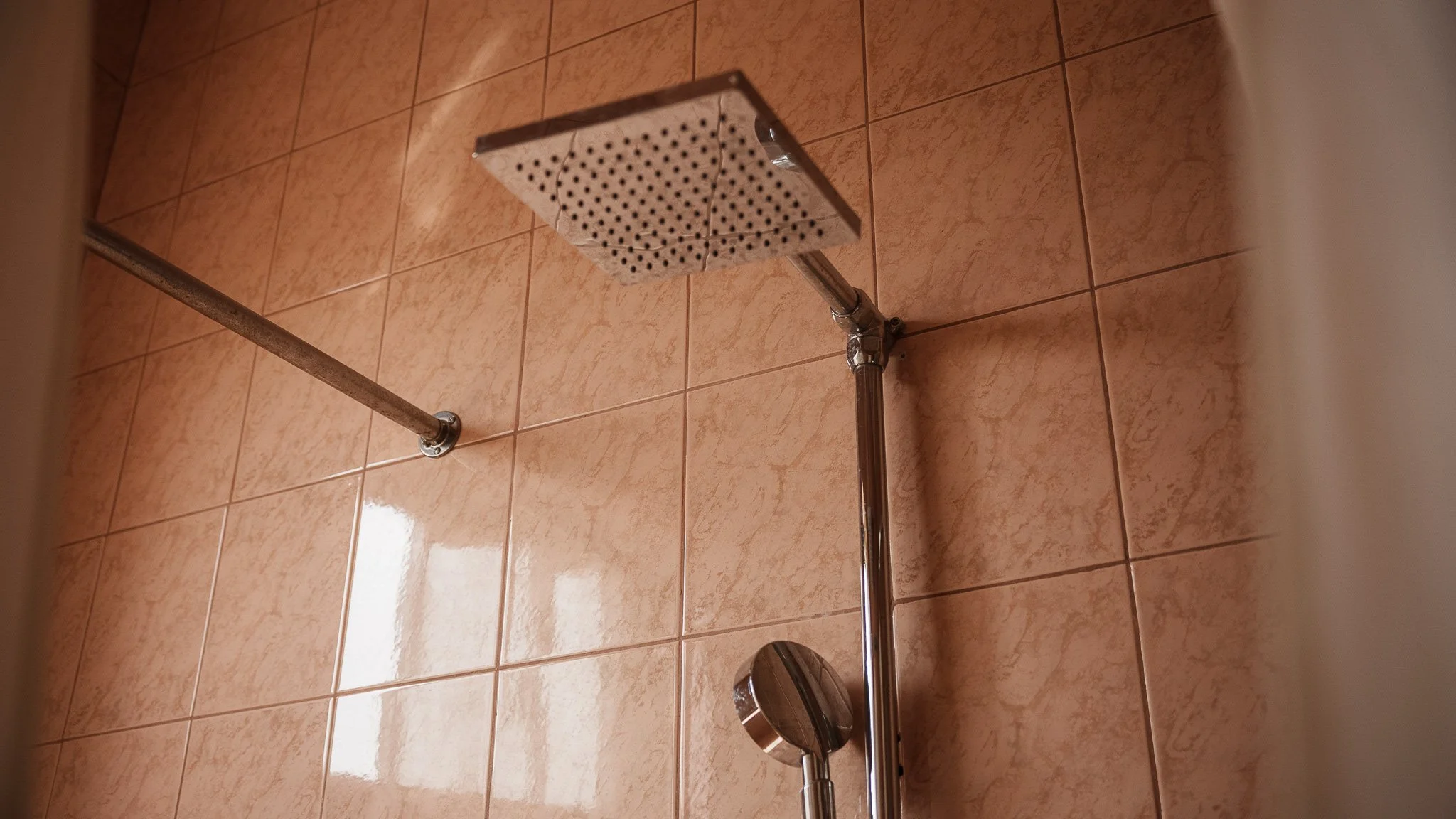 Close-up of a showerhead and a handheld shower wand mounted on a tiled bathroom wall with pinkish tiles at Quality Inn Hotel Kigali, Rwanda