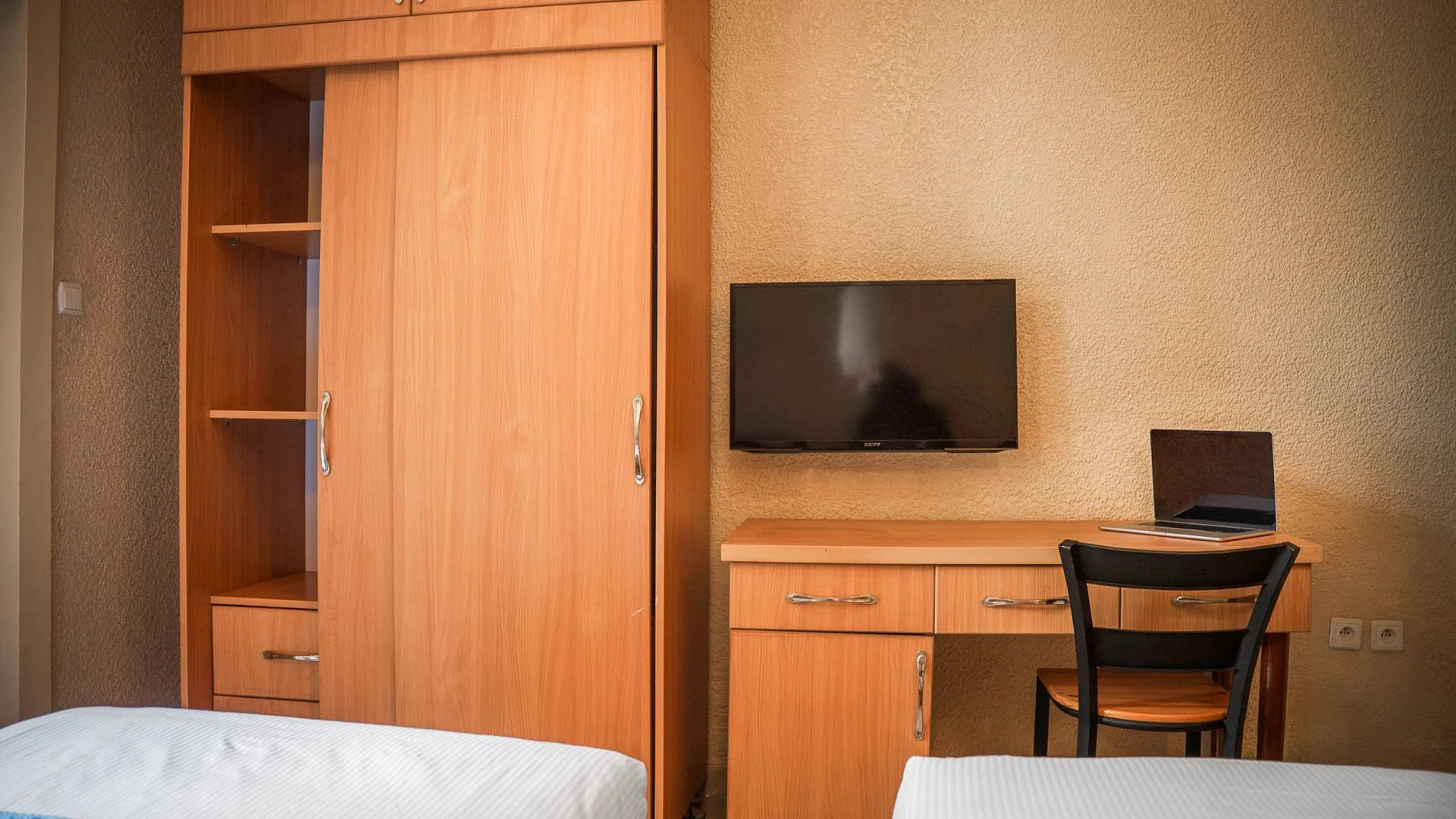 Deluxe Twin Room at Quality INN Hotel Kigali, Rwanda with wooden wardrobe, working desk with laptop, wall-mounted TV, and two beds with white bedding.