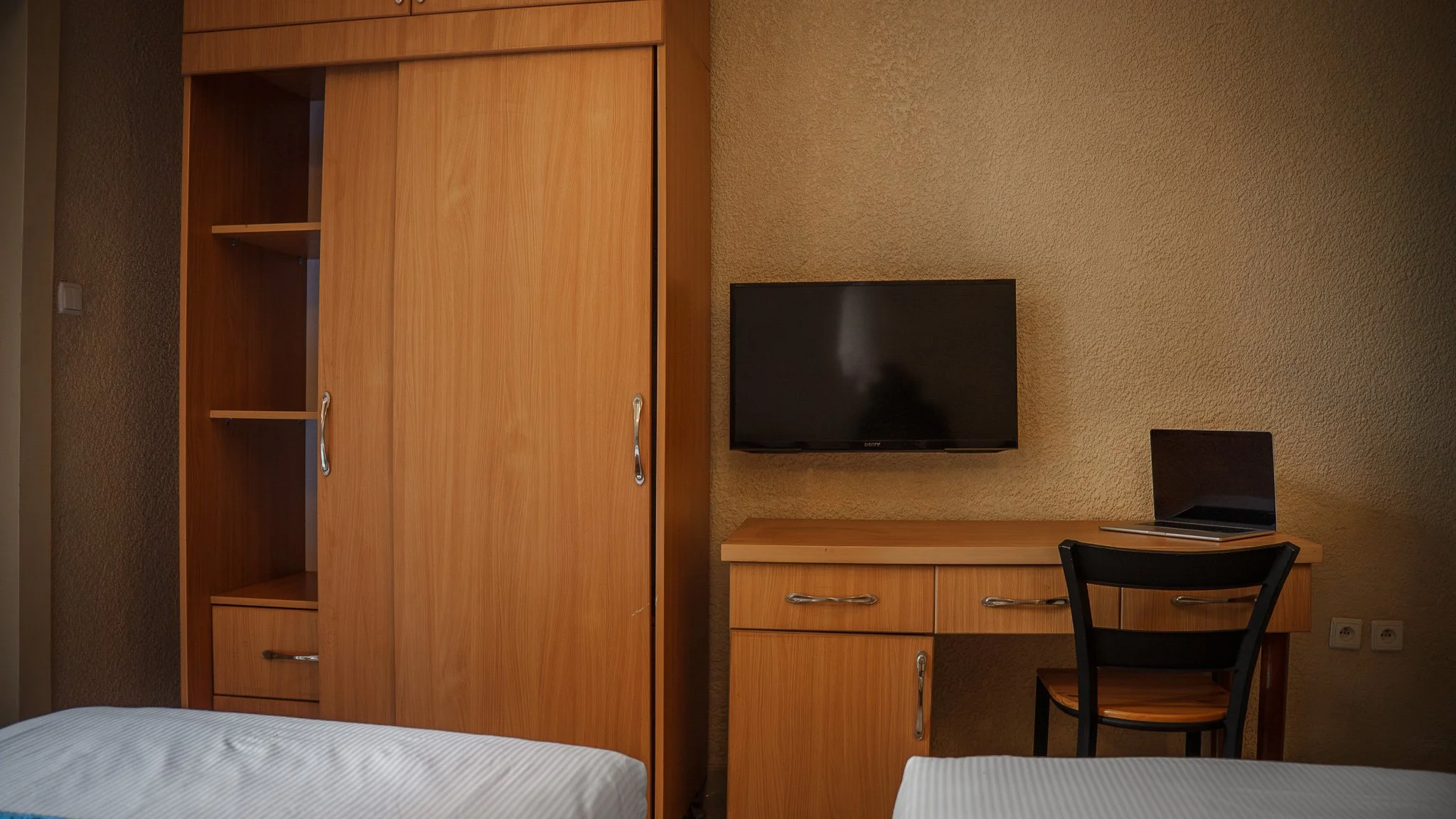 Deluxe Twin Room at Quality INN Hotel Kigali, Rwanda with wooden wardrobe, working desk with laptop, wall-mounted TV, and two beds with white bedding.