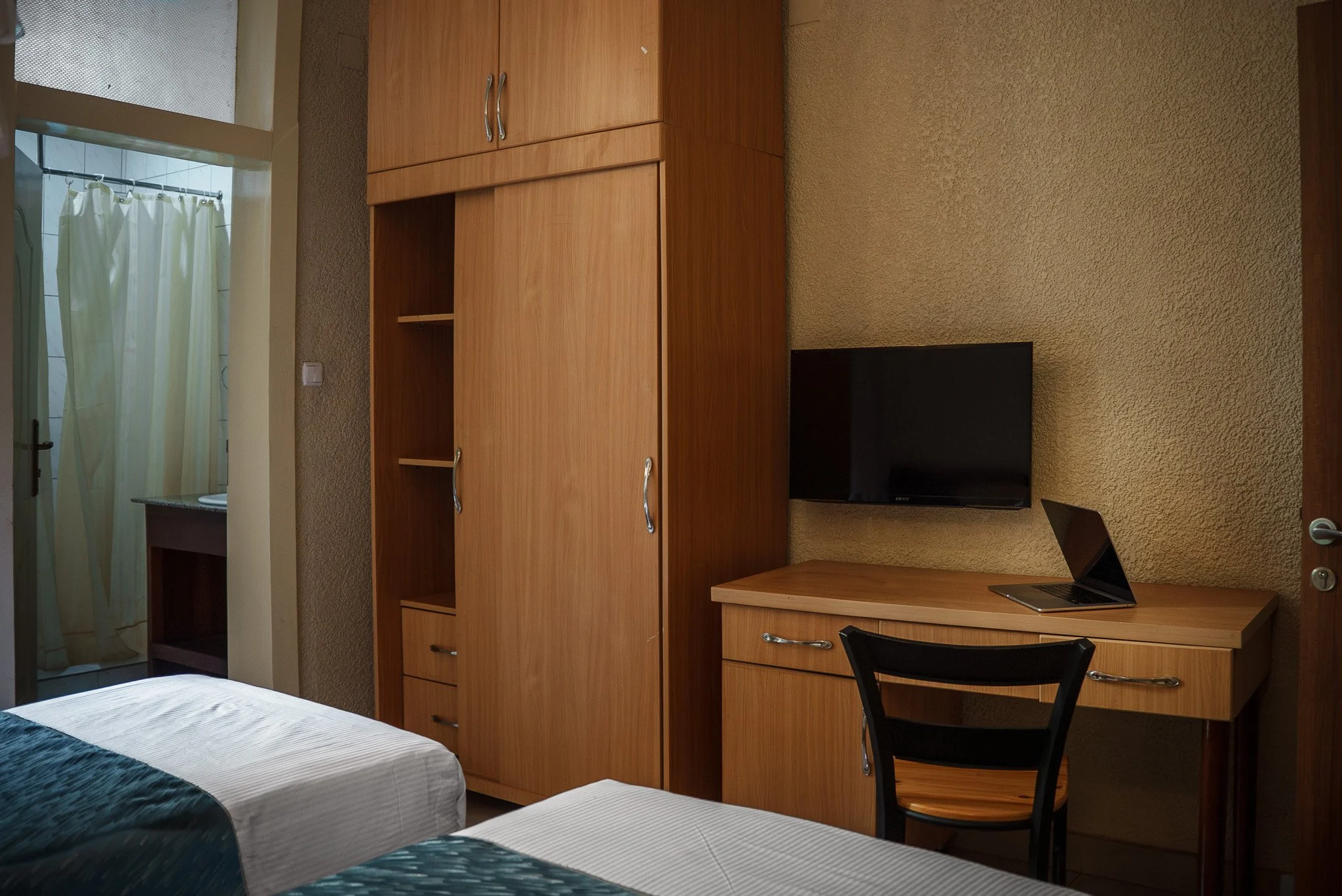 Deluxe Twin Room at Quality INN Hotel Kigali, Rwanda with wooden wardrobe, work desk with laptop and TV, bed, and bathroom with shower.