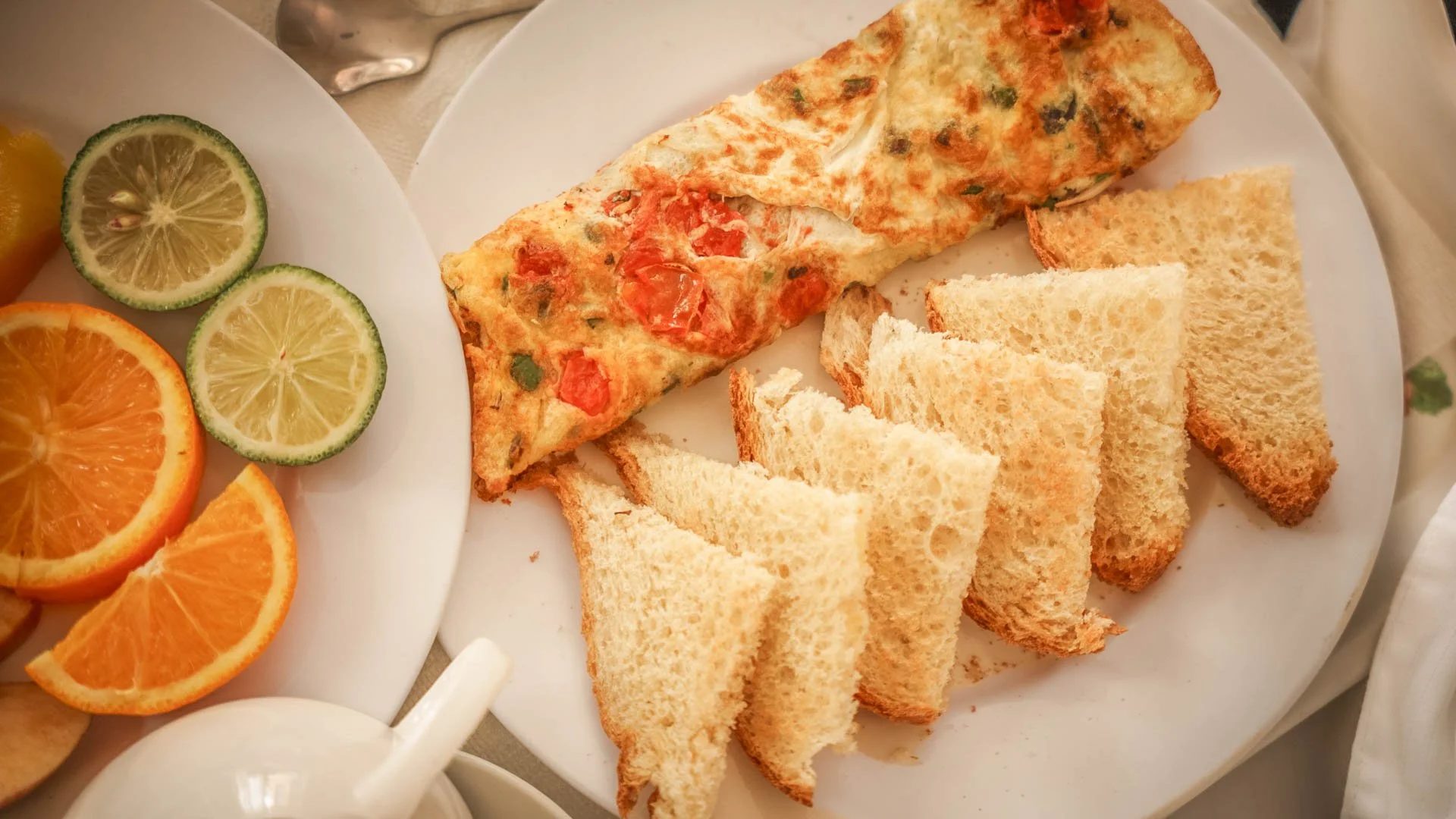 Breakfast with sliced oranges and limes, toasted sandwich, and omelette garnished with tomatoes and herbs, a quiet and relaxing morning dining experience at Quality Inn Hotel Kigali, Rwanda