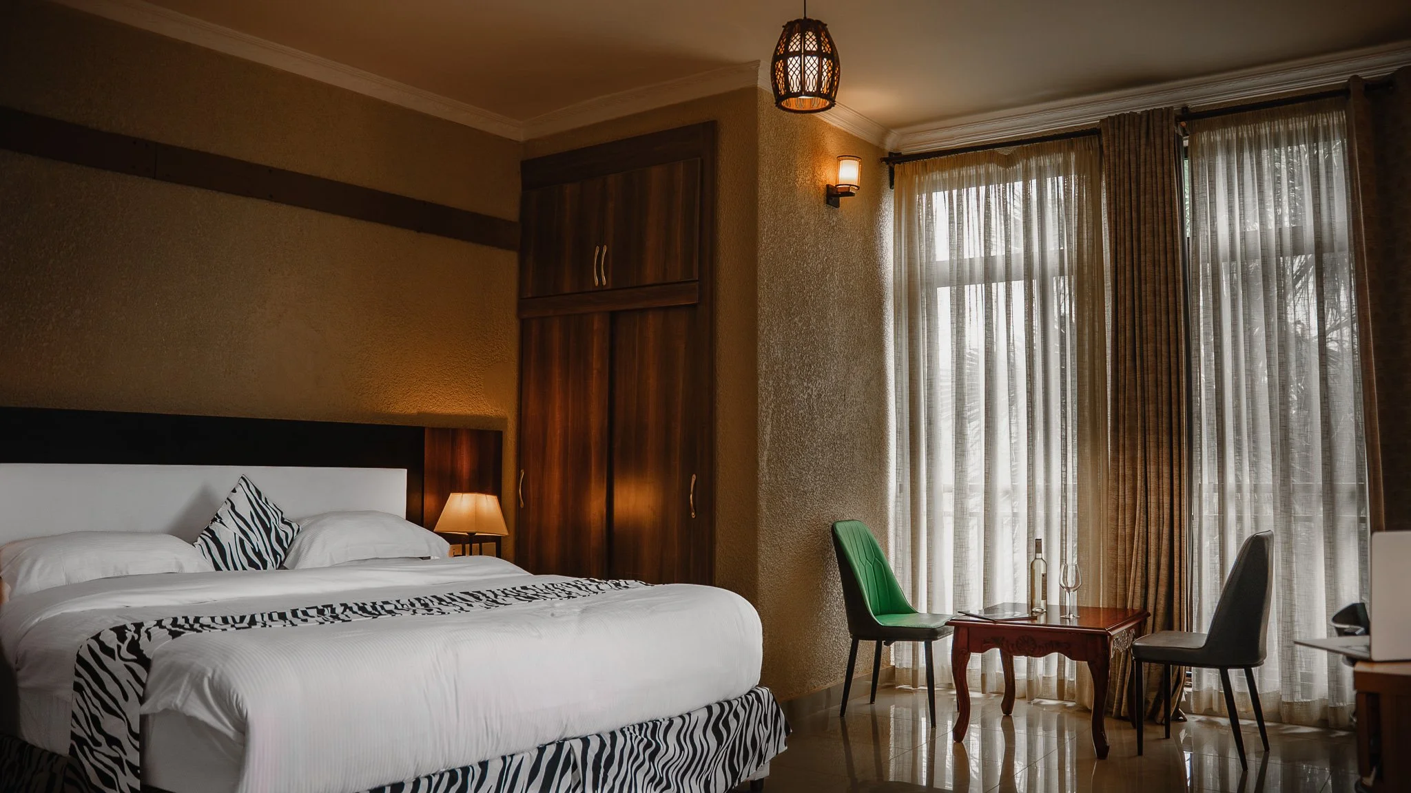Quiet, comfortable and spacious hotel room with white bedding, zebra print accent, seating area, and large windows, offering a relaxing stay at Quality Inn Hotel Kigali, Rwanda— ideal for couples, families, and business travelers.