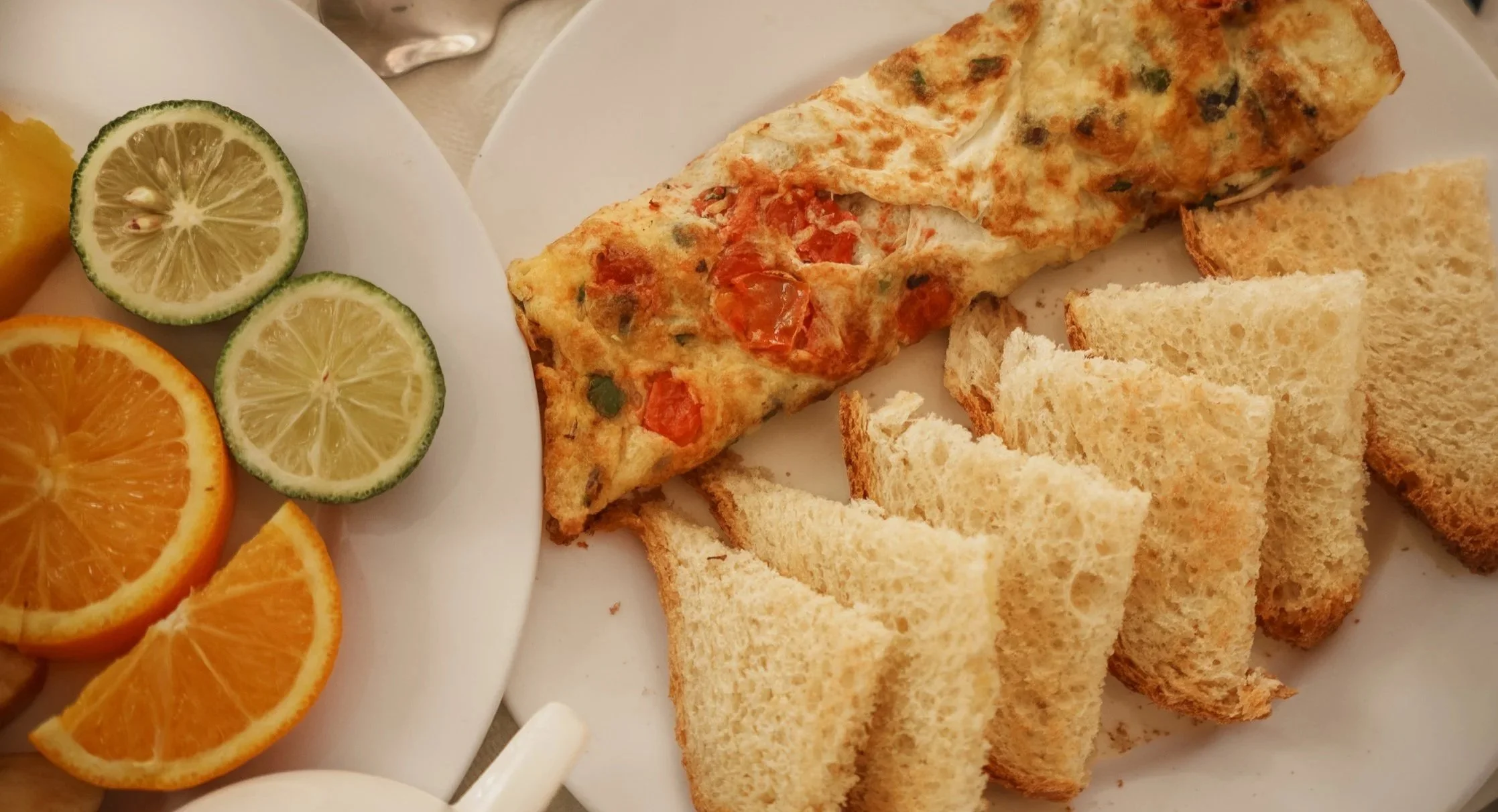Breakfast with sliced oranges and limes, toasted sandwich, and omelette garnished with tomatoes and herbs, a quiet and relaxing morning dining experience at Quality Inn Hotel Kigali, Rwanda