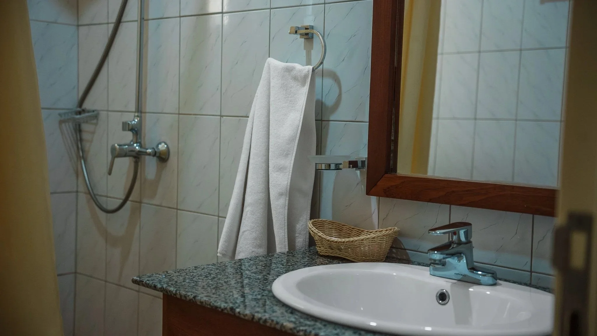Bathroom with a sink, mirror, soap dish, towel, shower area and tiled wall at Quality Inn Hotel Kigali, Rwanda.