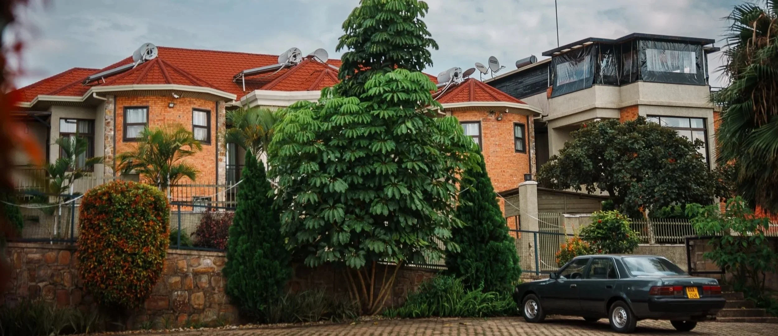 Quiet hotel in a calm Kigali neighborhood with red-roof buildings, lush garden trees and shrubs, and parking in front at Quality Inn Hotel Kigali, Rwanda