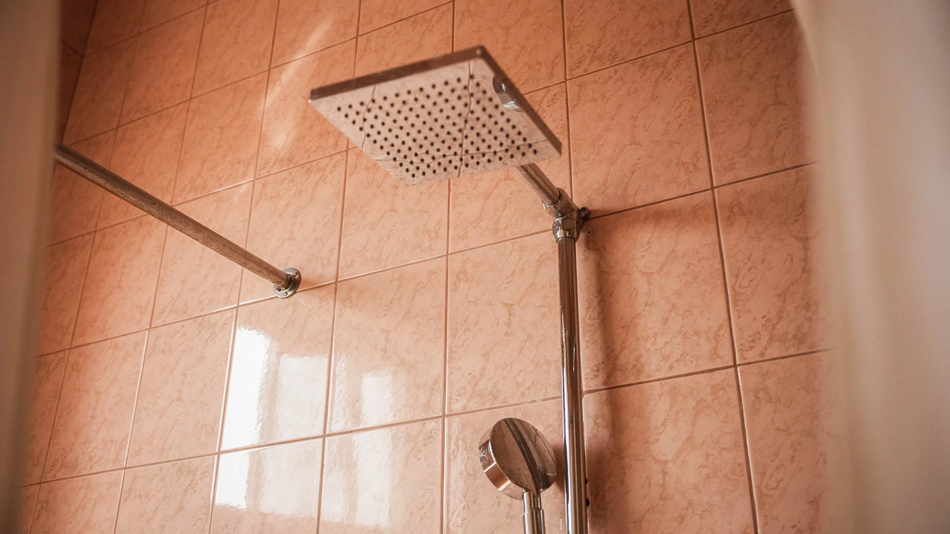 Close-up of a showerhead and a handheld shower wand mounted on a tiled bathroom wall with pinkish tiles at Quality Inn Hotel Kigali, Rwanda