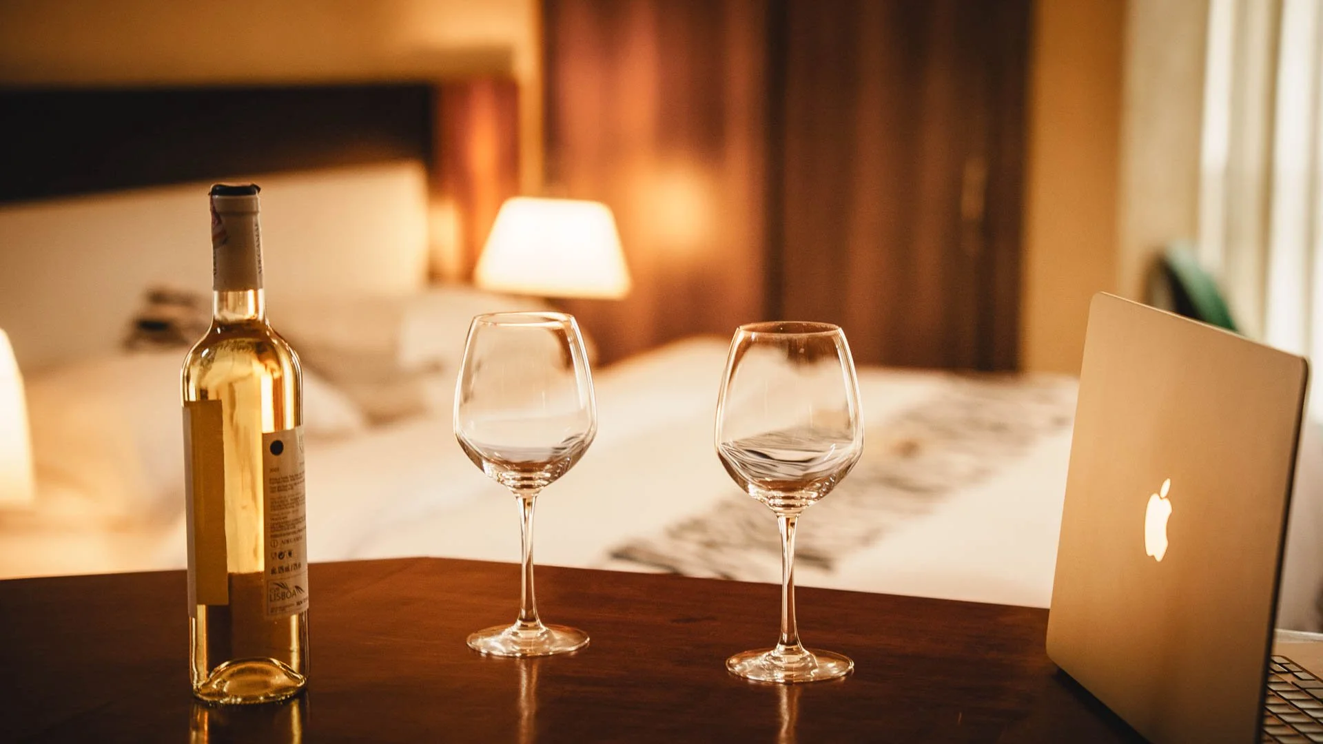 Cozy hotel room at Quality Inn Hotel Kigali, Rwanda, with warm lighting, a comfy bed, table with white wine, two glasses, and an open MacBook—perfect for a quiet night with fine wine and finer company.