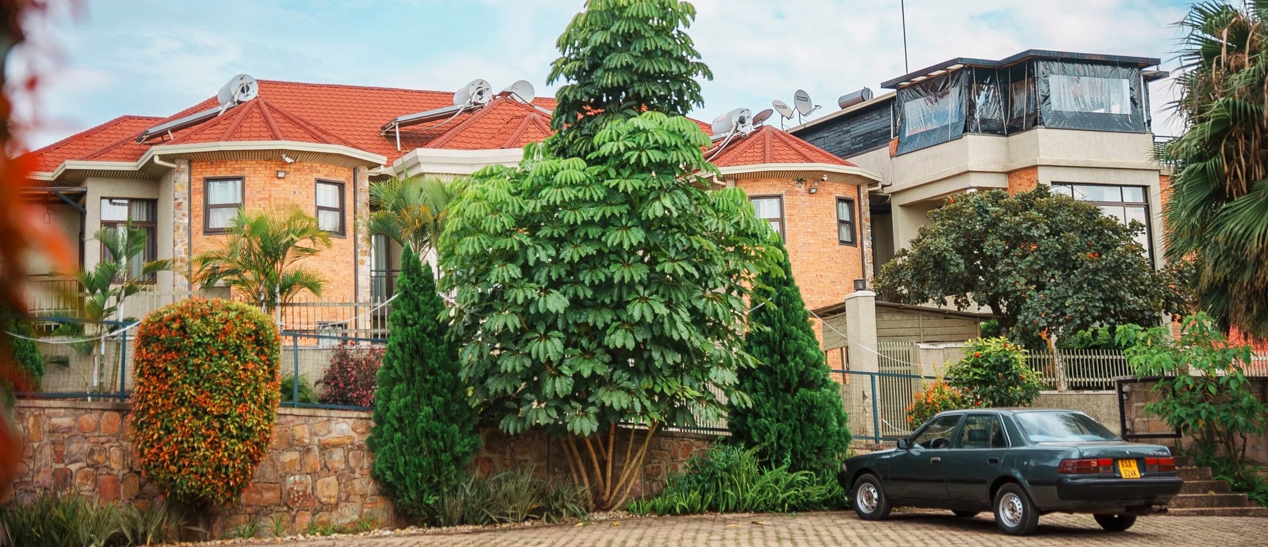 Quiet hotel in a calm Kigali neighborhood with red-roof buildings, lush garden trees and shrubs, and parking in front at Quality Inn Hotel Kigali, Rwanda