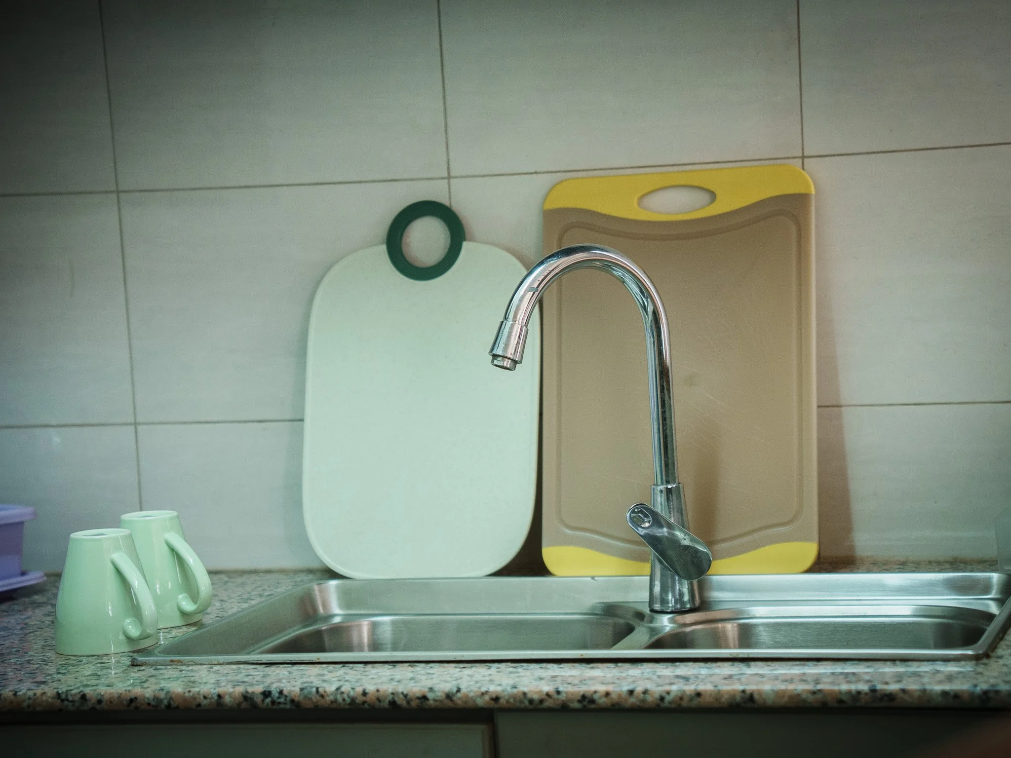 Kitchen sink in the king studio kitchenette at Quality INN Hotel Kigali, Rwanda, with chrome faucet, green cups, and colorful cutting boards.