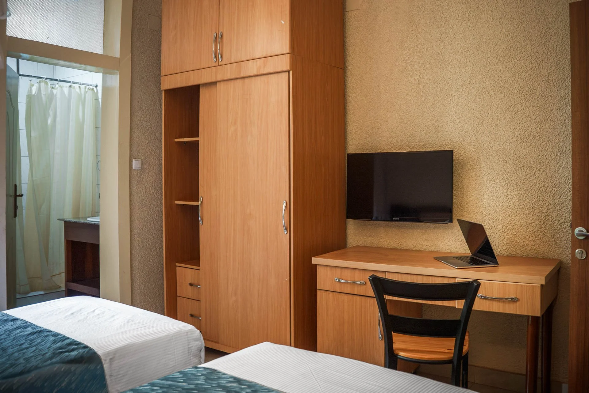 Deluxe Twin Room at Quality INN Hotel Kigali, Rwanda with wooden wardrobe, work desk with laptop and TV, bed, and bathroom with shower.