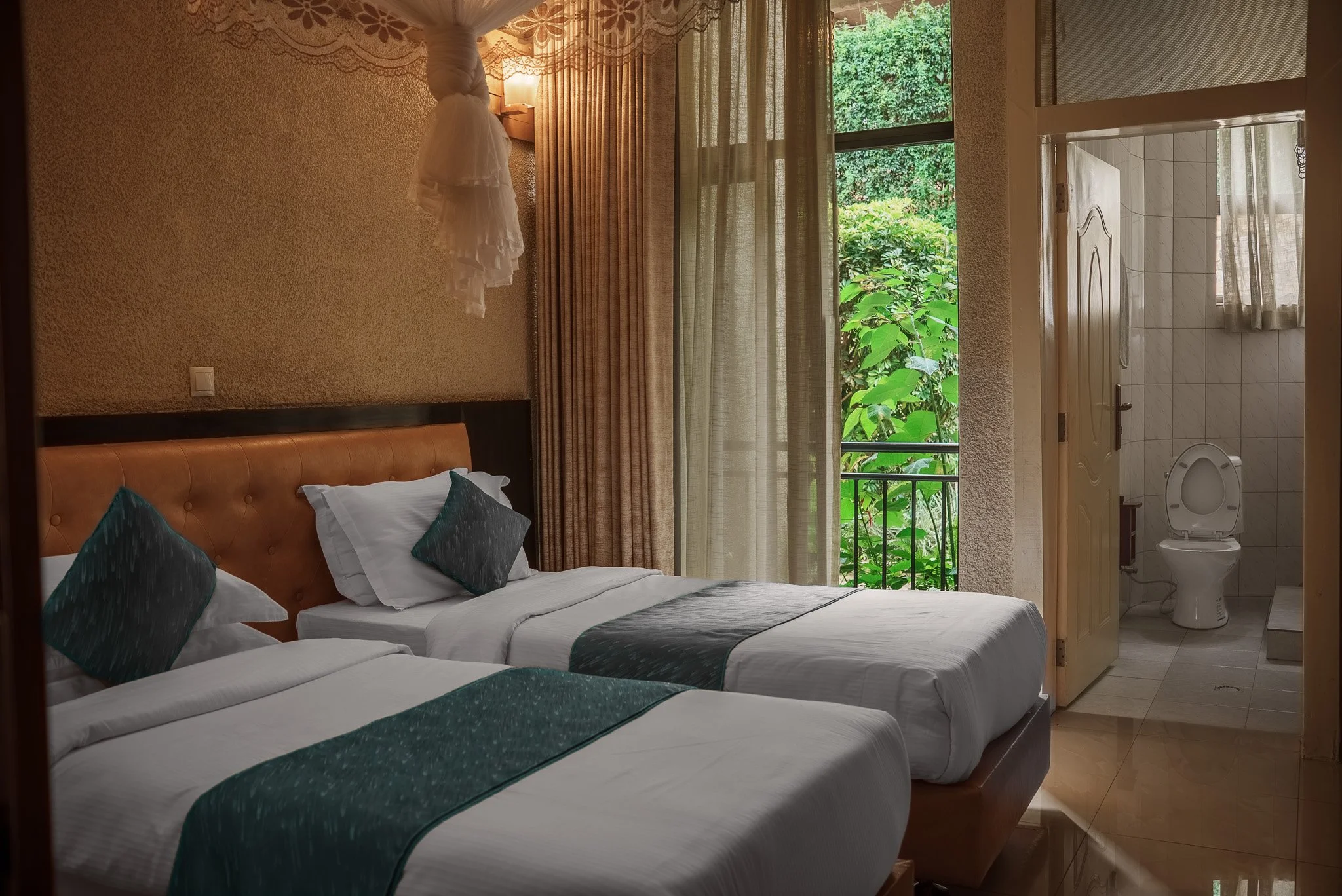 Deluxe Twin room at Quality Inn Hotel Kigali in Rwanda with two separate twin beds, warm lighting, a window with beige curtains overlooking lush greenery, and a private bathroom—quiet and suitable for friends or business travelers.