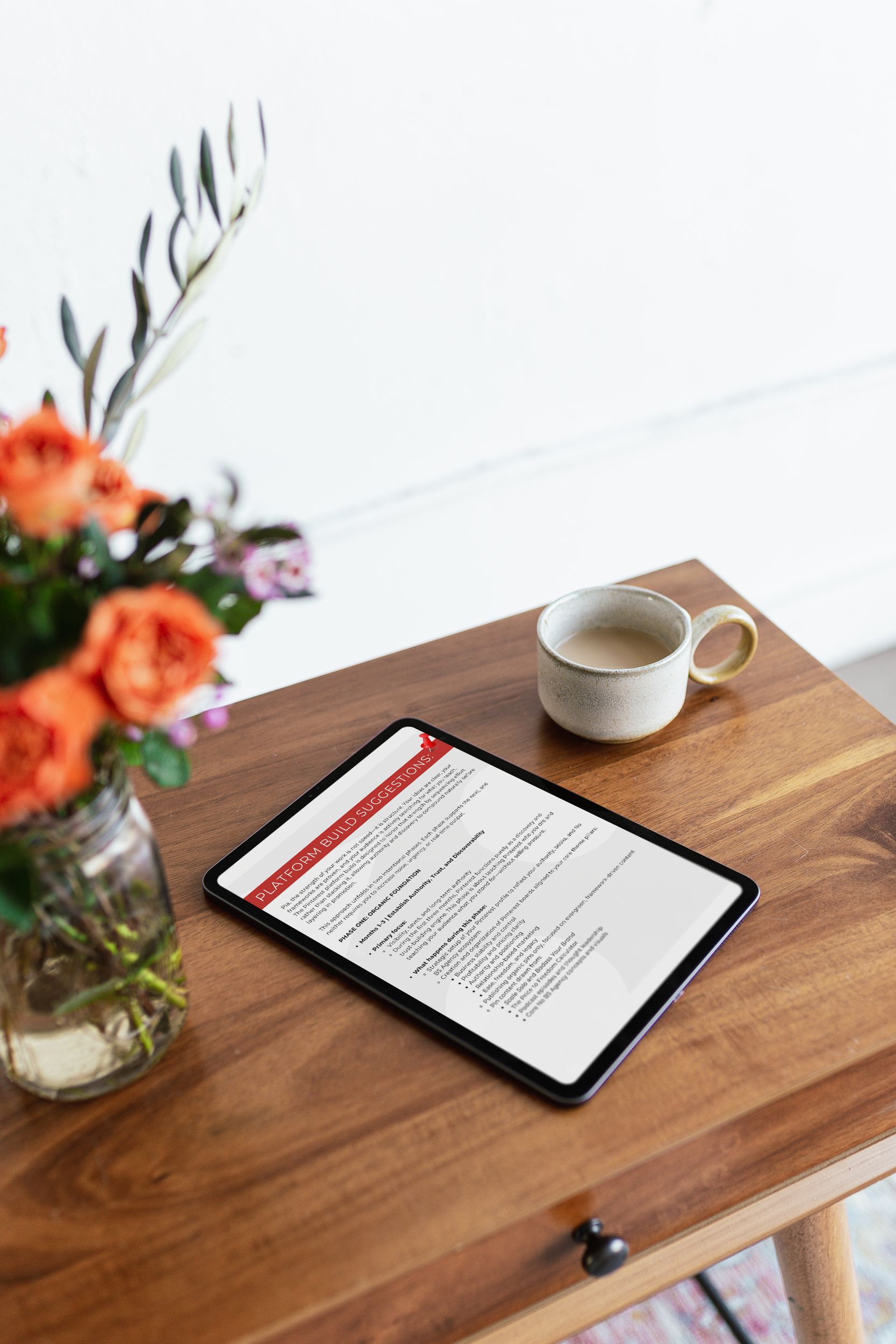 Tablet displaying a document titled 'Platform Build Suggestions' on a wooden table next to a coffee cup and a vase of colorful flowers.