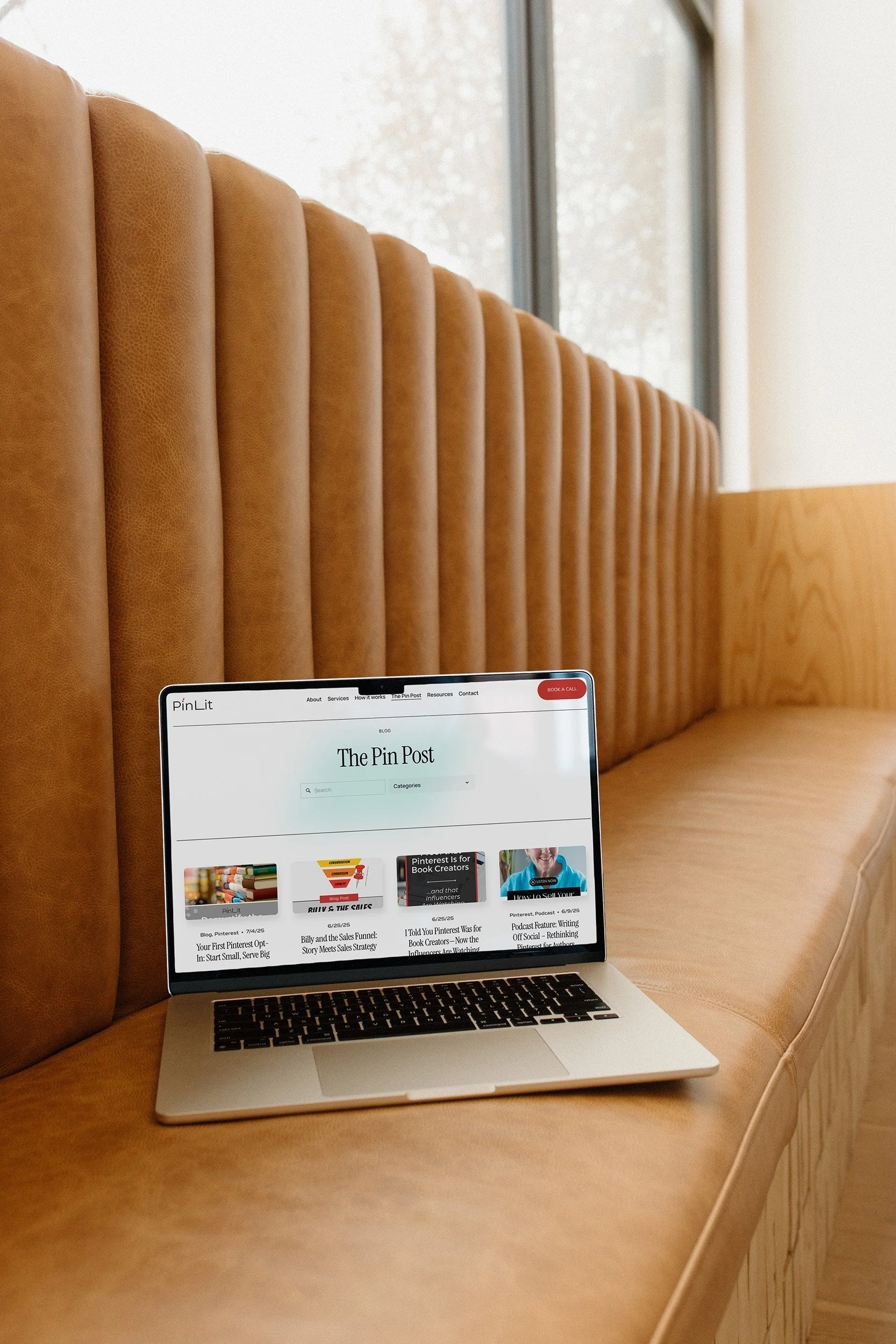 A laptop on a tan leather booth seat displaying a blog webpage called The Pin Post.