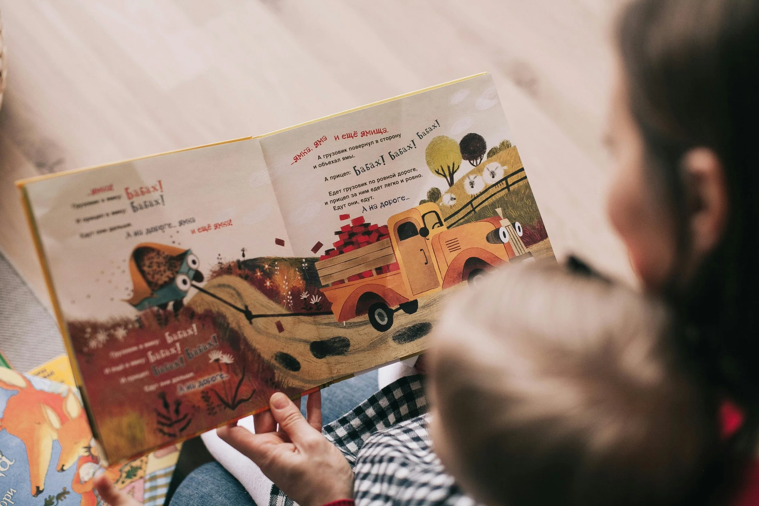 A child with glasses reading a colorful illustrated children's book with a truck carrying bricks on a dirt road.