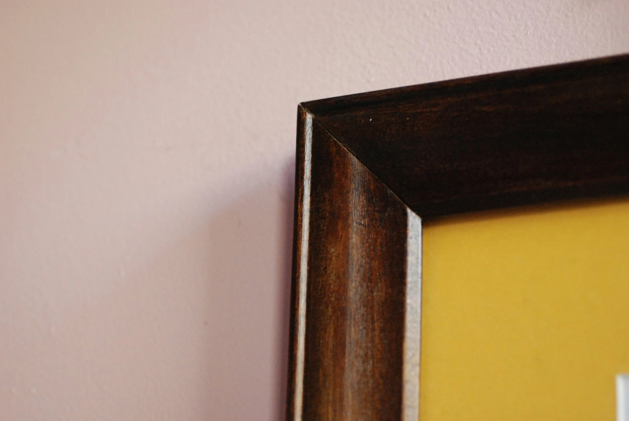 Close-up of a dark wooden picture frame corner against a pale pink wall.