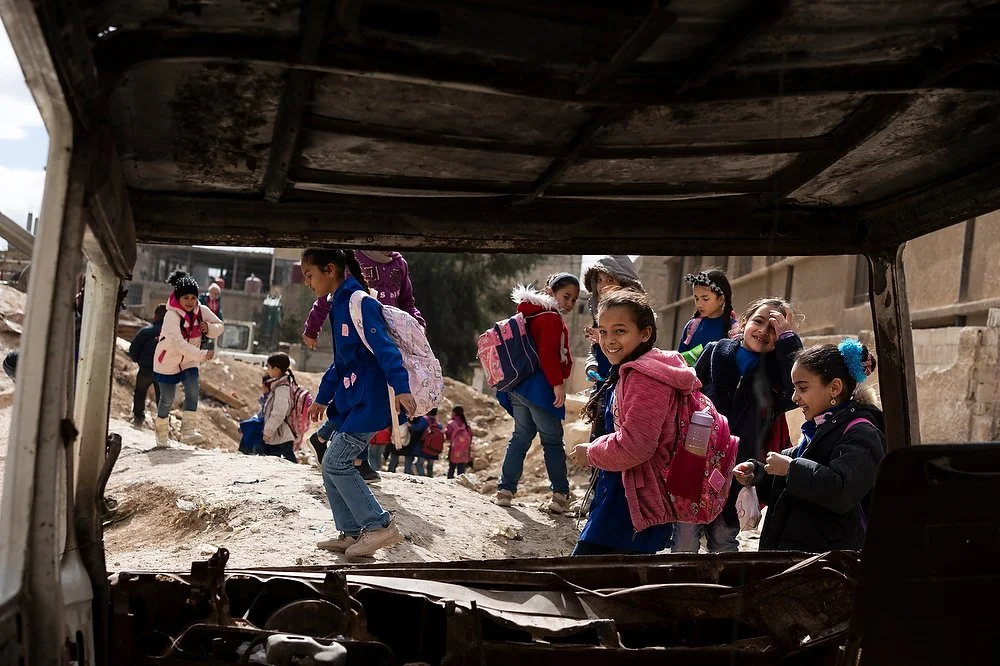 A group of girls outside the Palestinian house Mjedel School in Syria, Damascus viewed through the window of an abandoned vehicle.