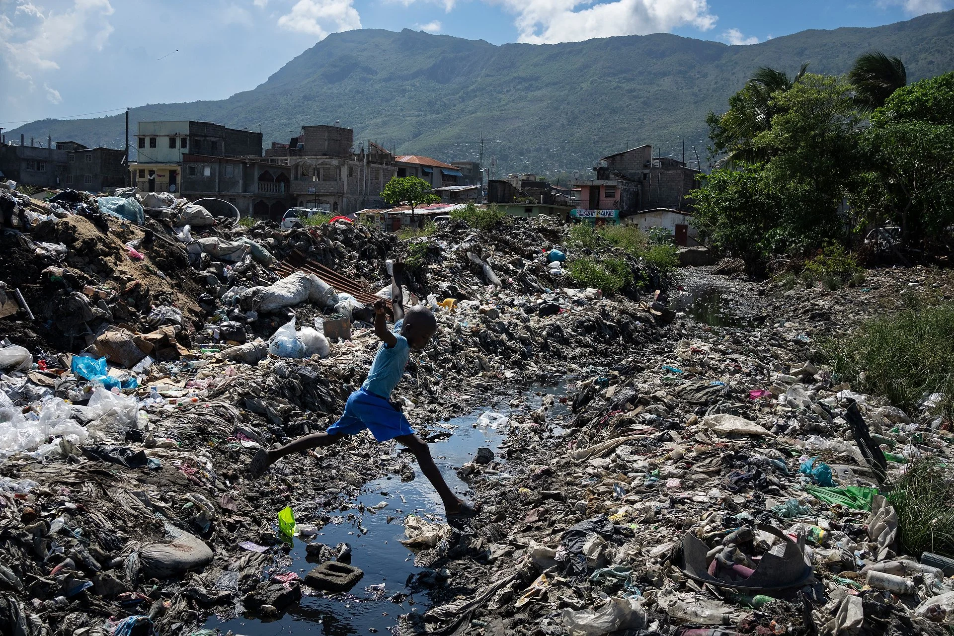Young boy leaps over piles of accumulated waste in Cap-Haitien, Haiti.
