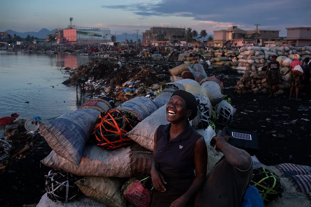 A women standing in front of bags of charcoal laughs at a market in Cap-Haïtien where charcoal made from mangrove wood is sold.