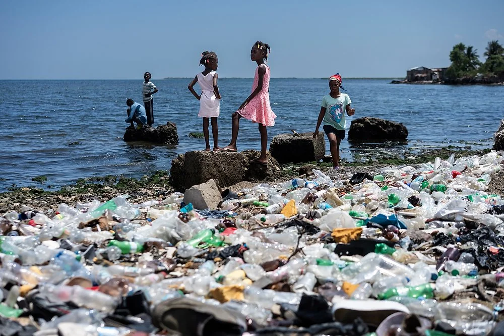 People standing on a shoreline covered in plastic waste in Cap Haitien
