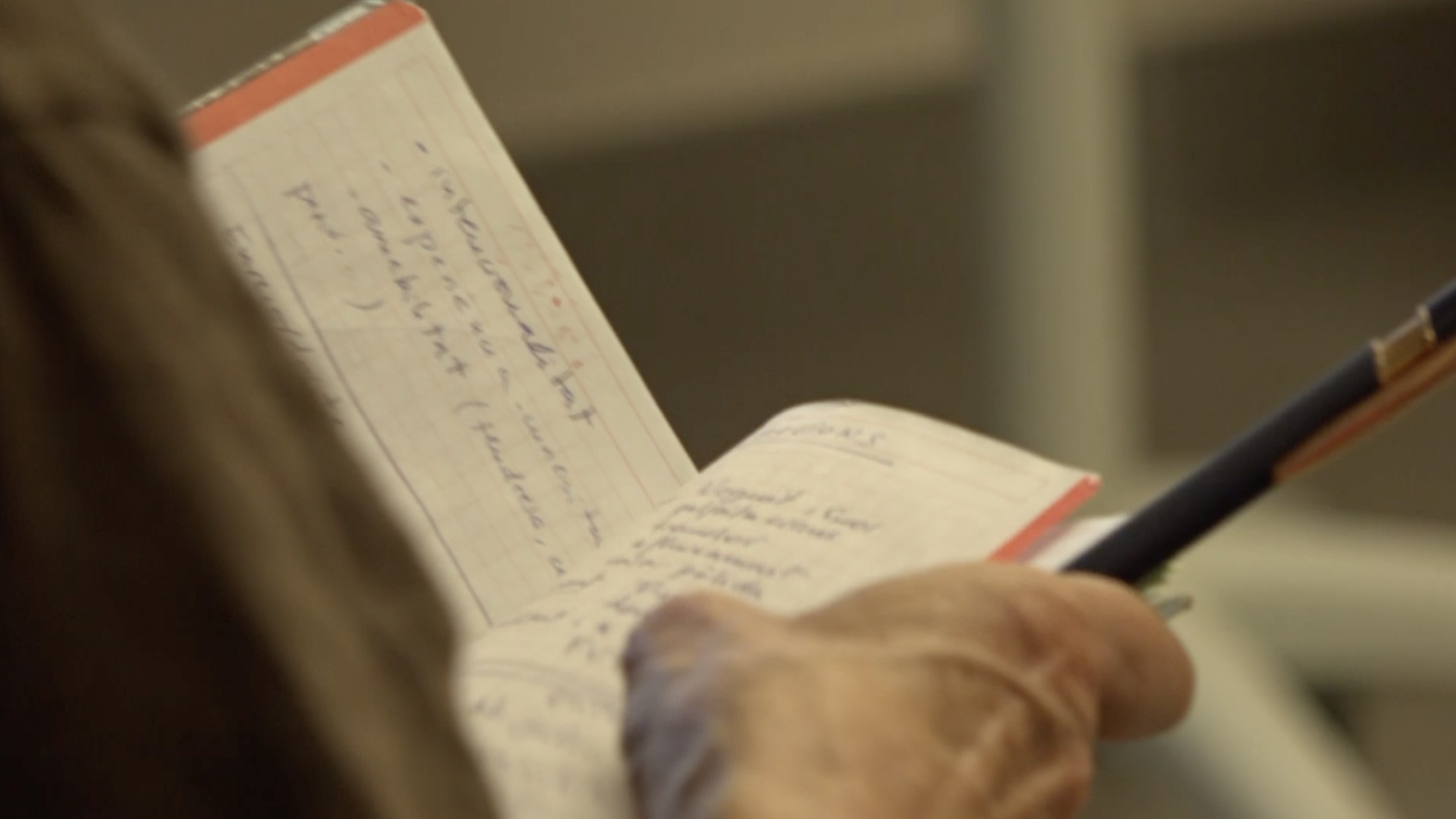 Close-up of a person writing in a notebook with a black pen, with handwritten text visible on the pages.