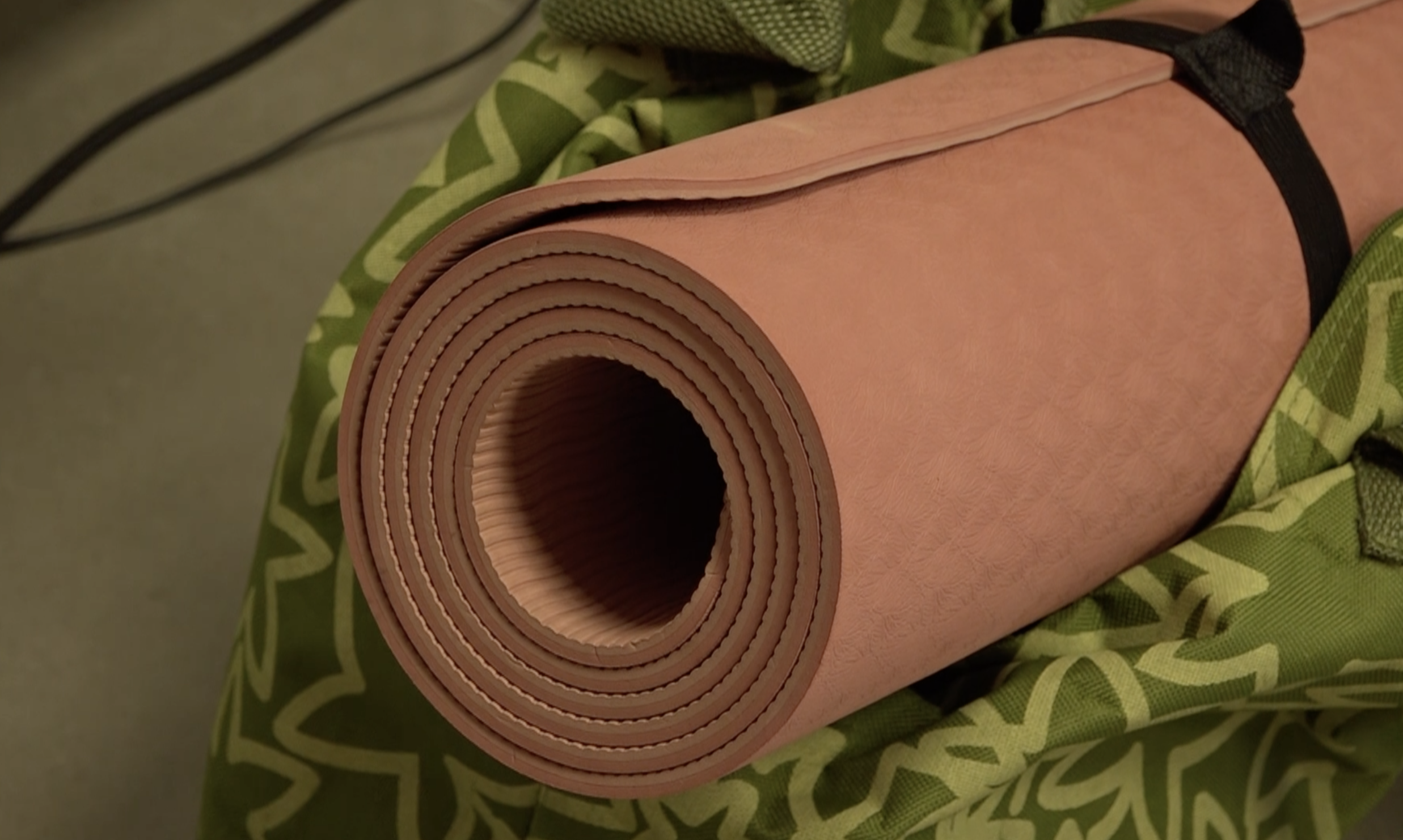 A rolled pink yoga mat resting on a green patterned yoga bag.