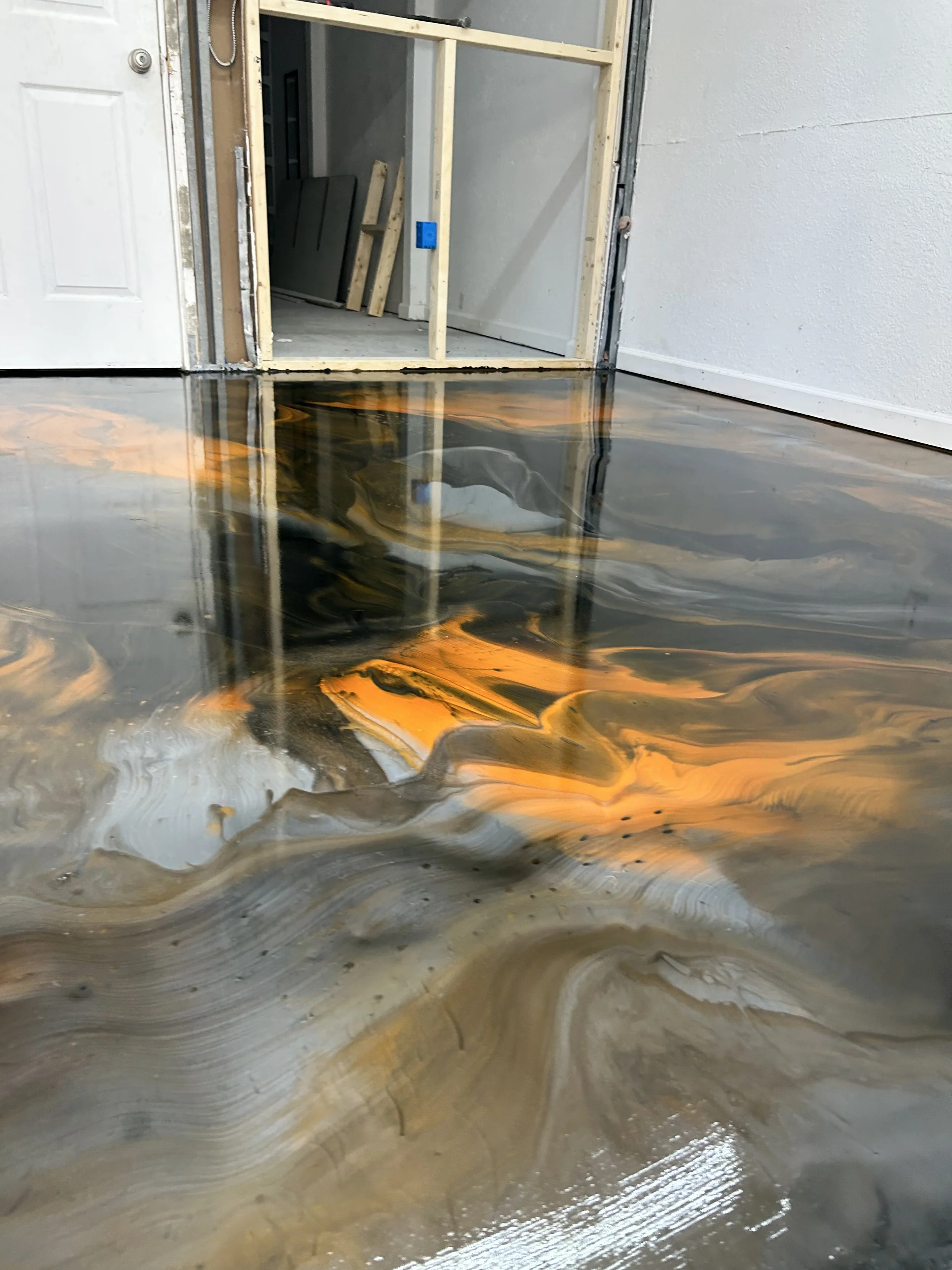 Mettalic  epoxy floor with swirling patterns of orange, black, and gray paint reflections, partially inside a room with construction space visible.