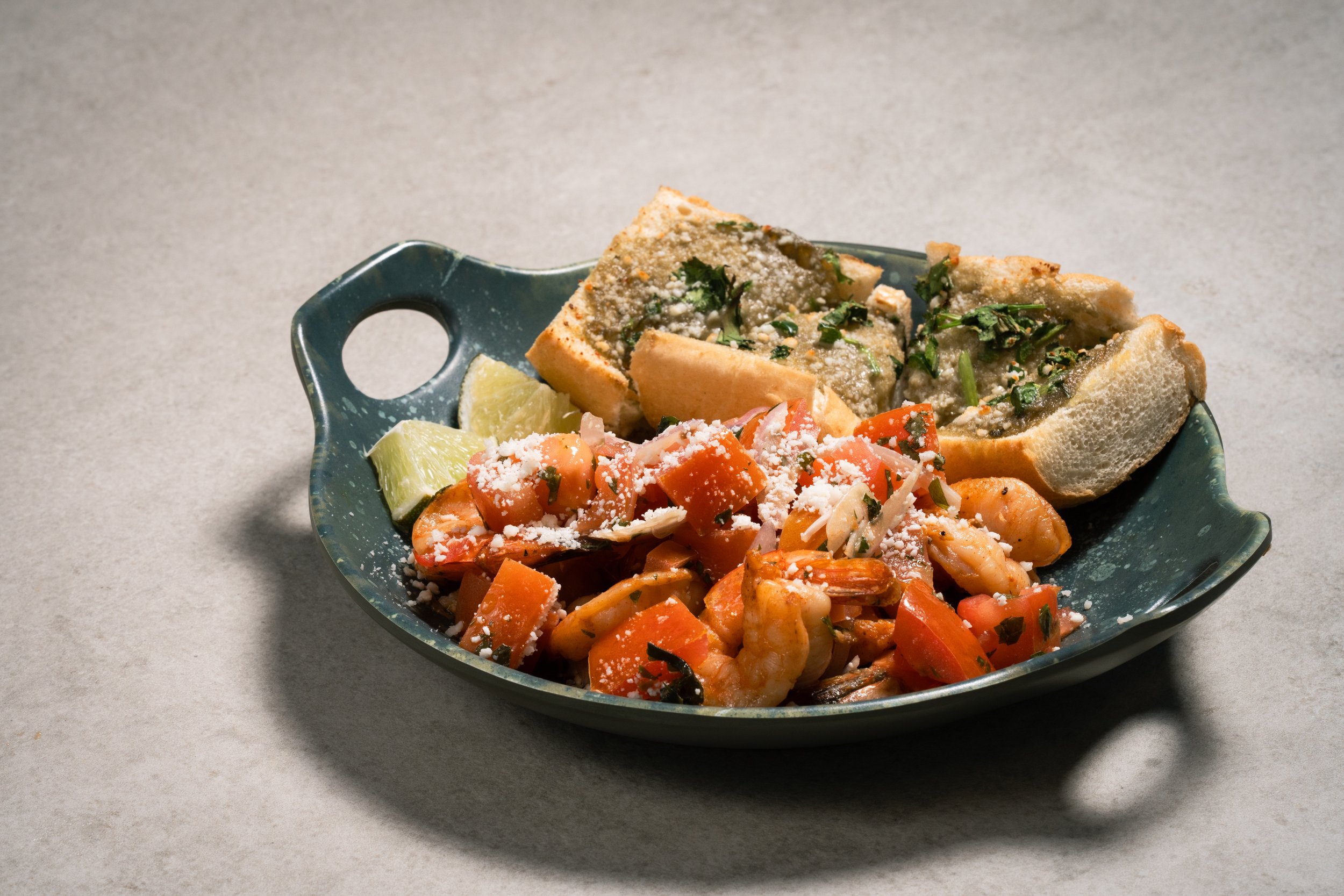 A blue ceramic dish with white mexican shrimp, toast topped with herbs, lime wedges. 
