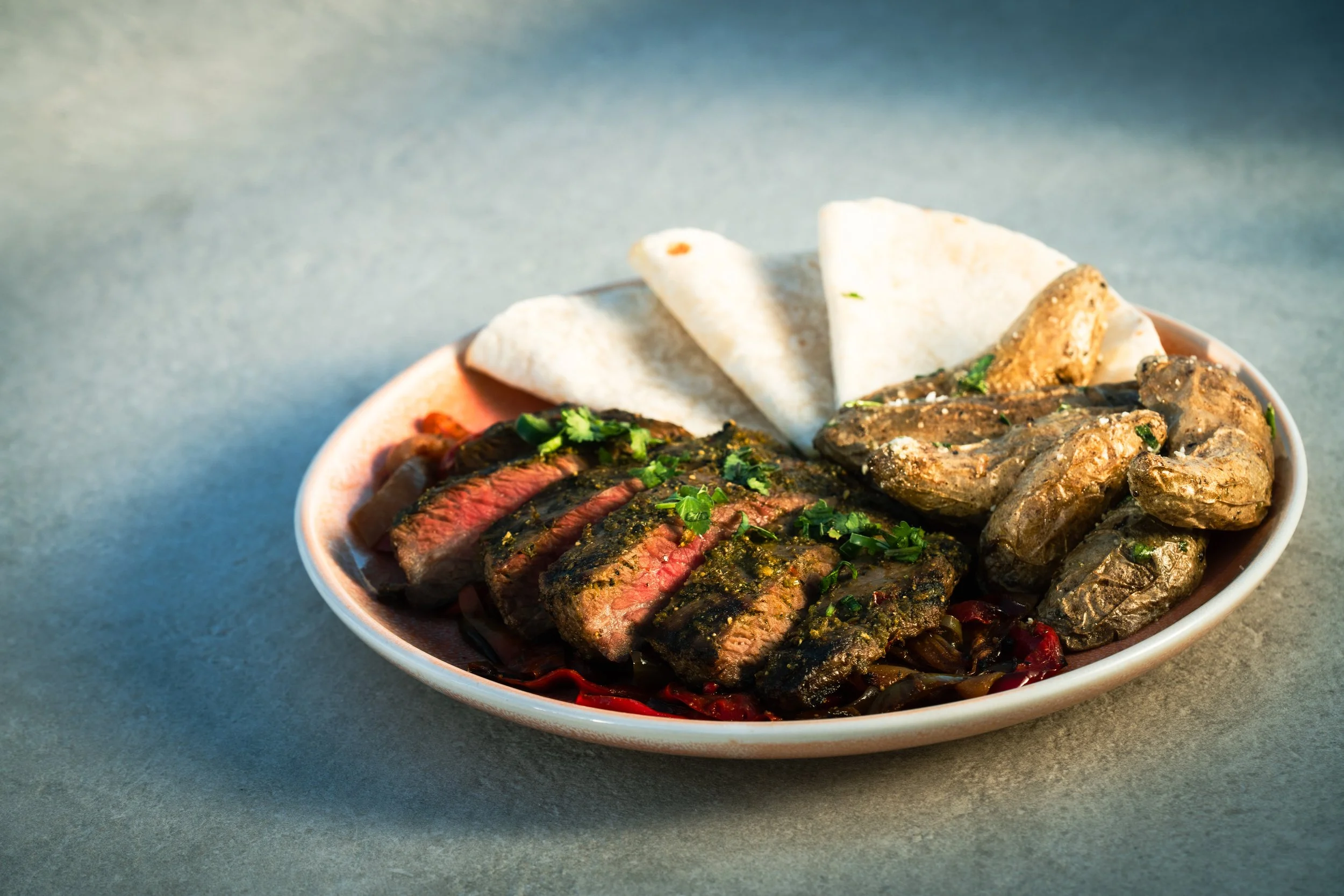 A bowl of flank steak, arrachera salsa, onion, peppers, cilantro, black garlic and huitlacoche papas.