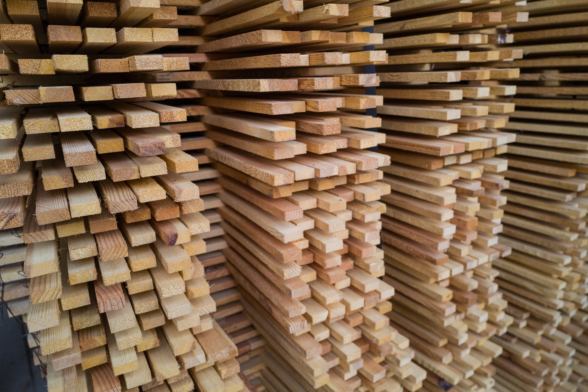 Stacked wooden lumber boards in a close-up view, showing sawn edges and grain for construction materials.