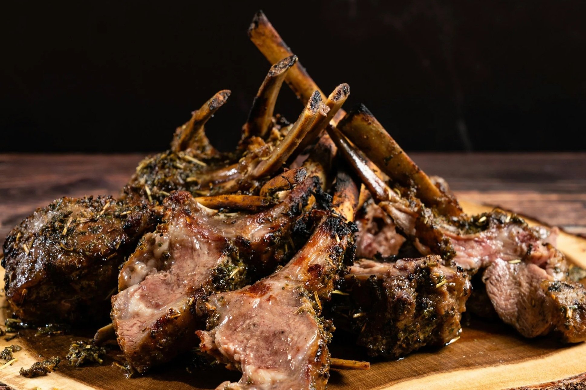 Cooked lamb chops with herbs on a wooden cutting board.
