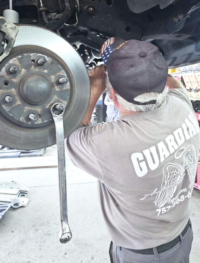 A person working on a car's brake system, using a wrench while under the vehicle in an automotive repair shop.