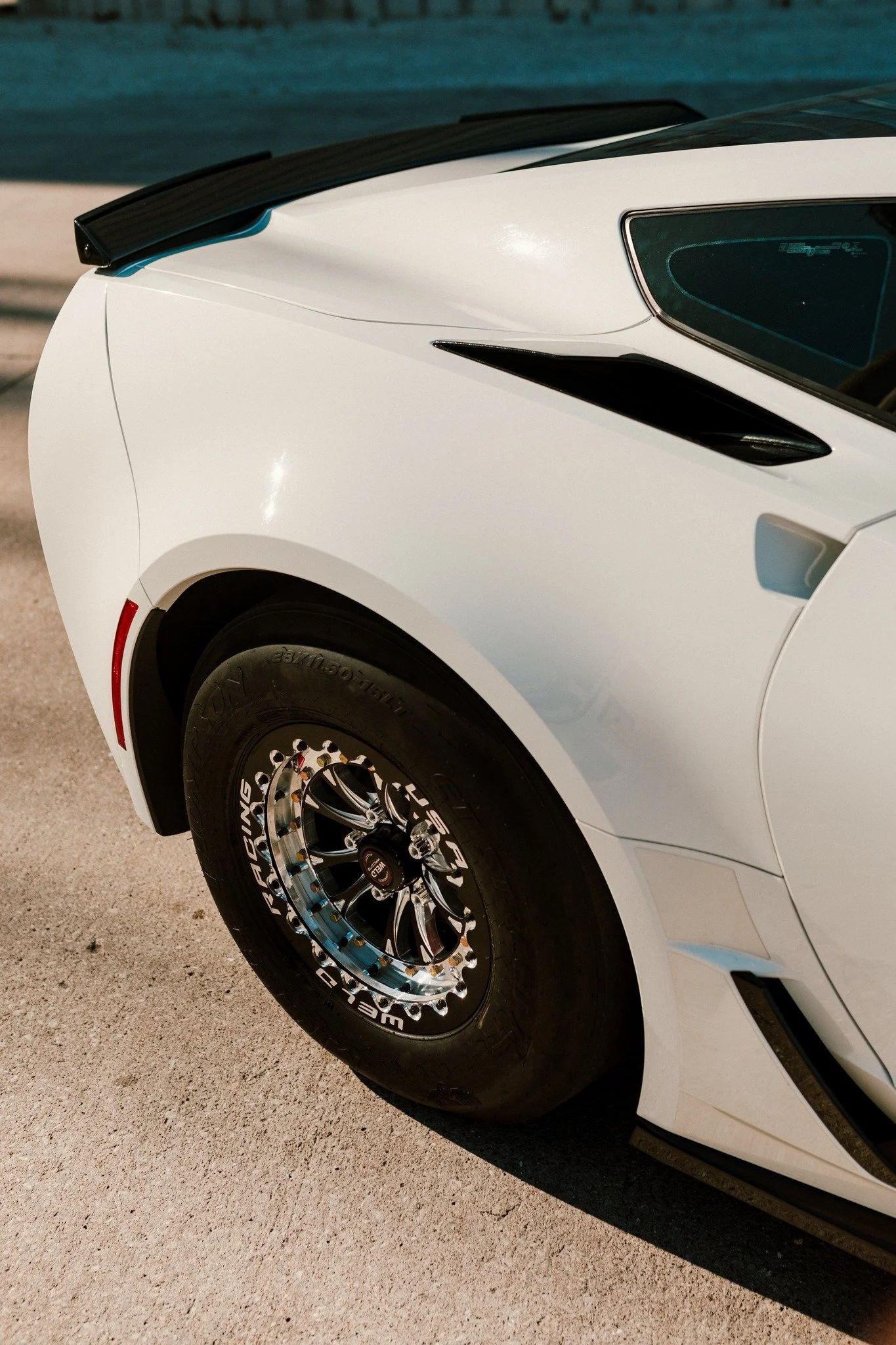 Close-up of the front side of a white sports car showing the wheel, tire, and part of the hood.