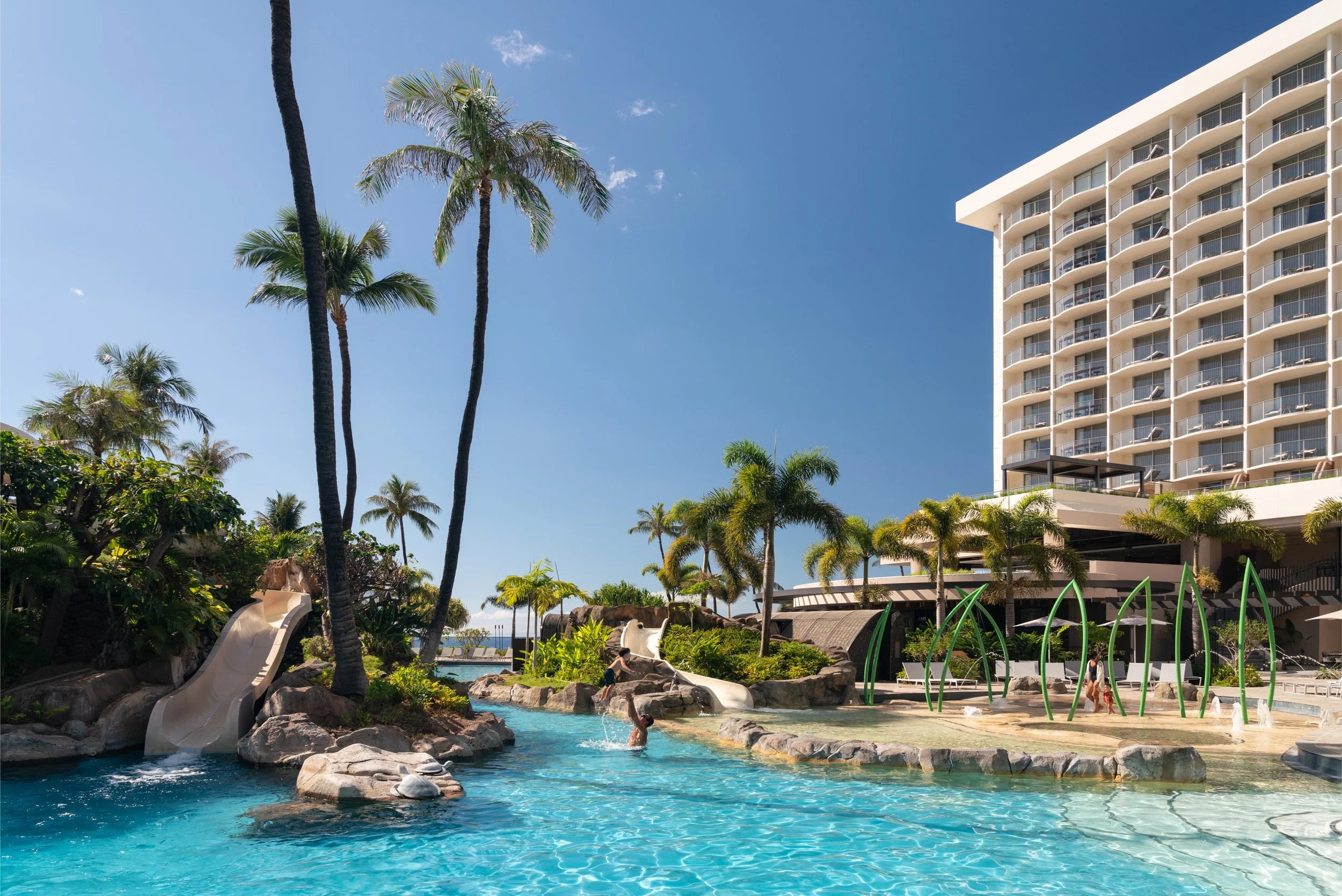 Inground pool with water slide, palm trees, and luxury hotel
