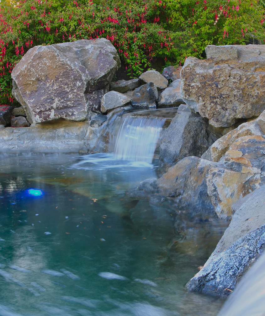 Natural stone wall with sleek waterfall and pool lighting