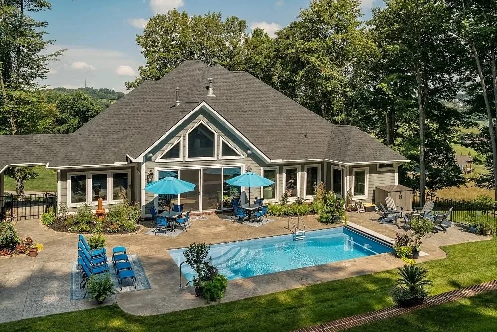 Inground pool patio with lush, green plantings and blue umbrellas
