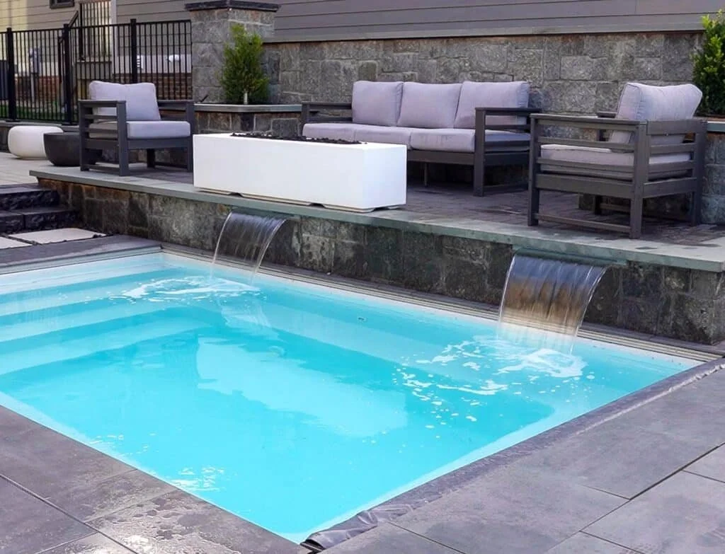 Outdoor backyard with a small swimming pool and waterfall feature, surrounded by patio furniture including a sofa and armchairs.
