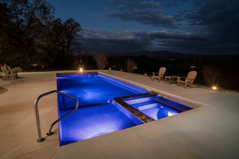 Inground pool and integrated spa with outdoor lighting at night