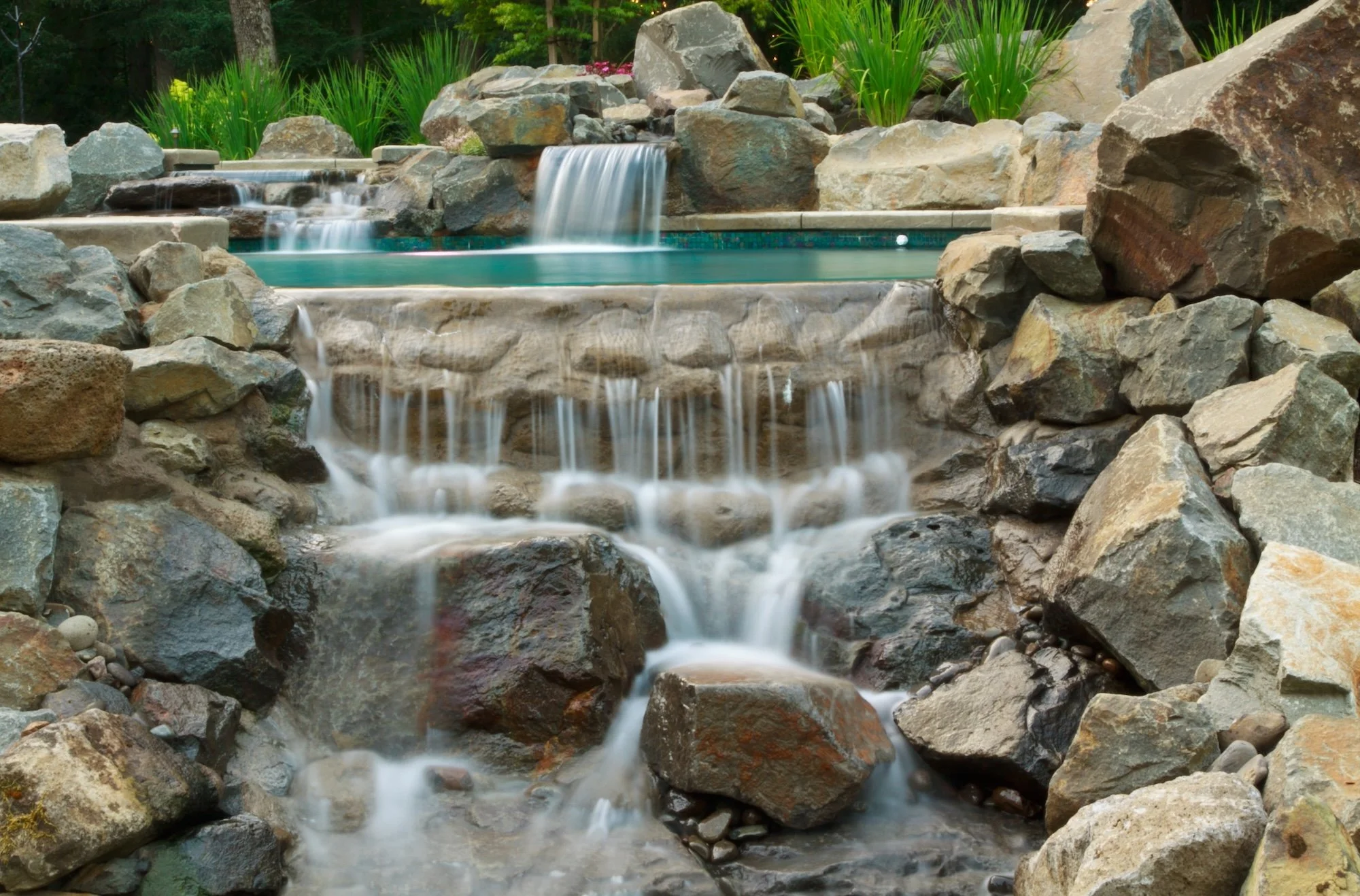 A waterfall flowing over rocks into a pond surrounded by large stones and greenery.