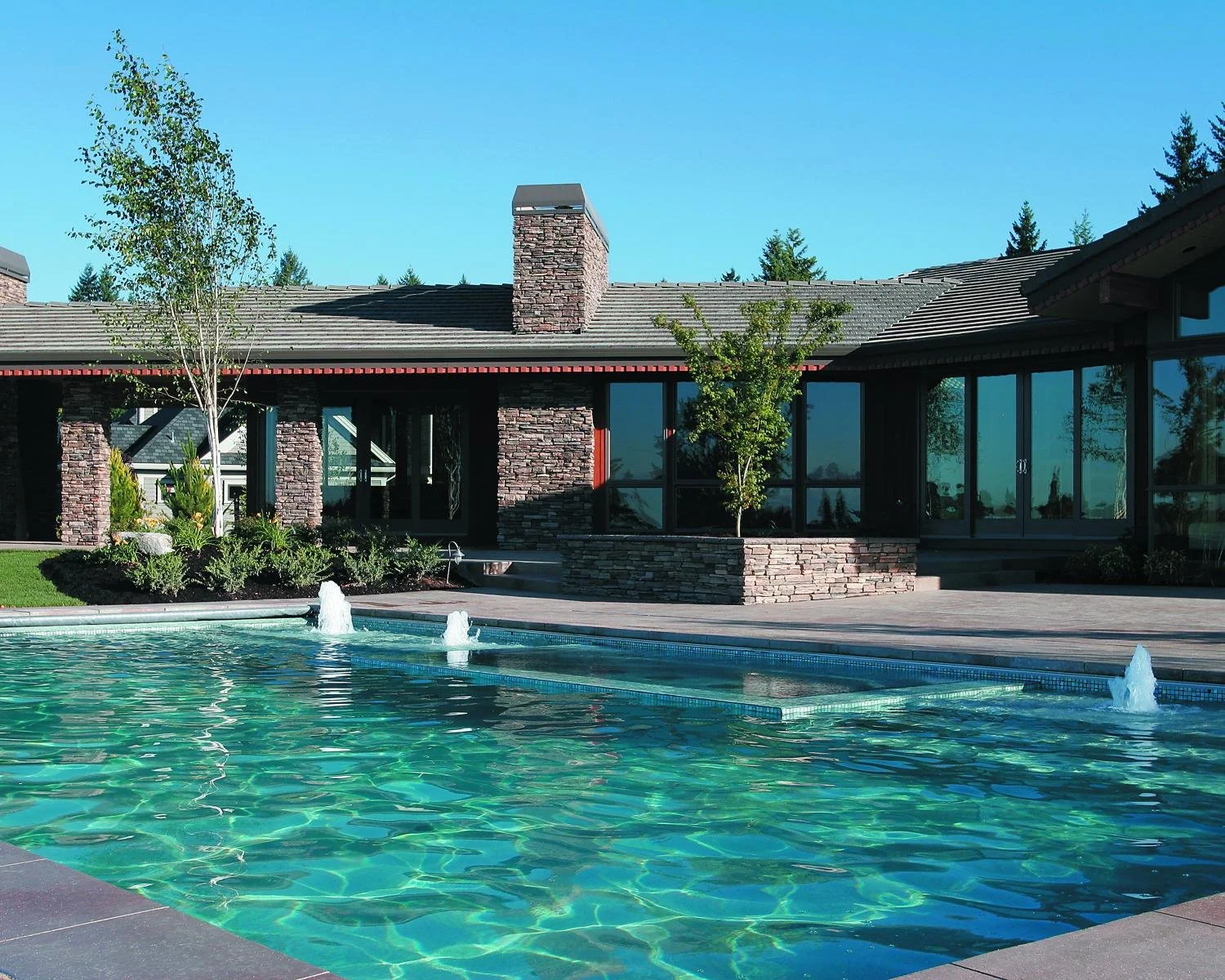Fiberglass inground pool with water features and stone retaining wall