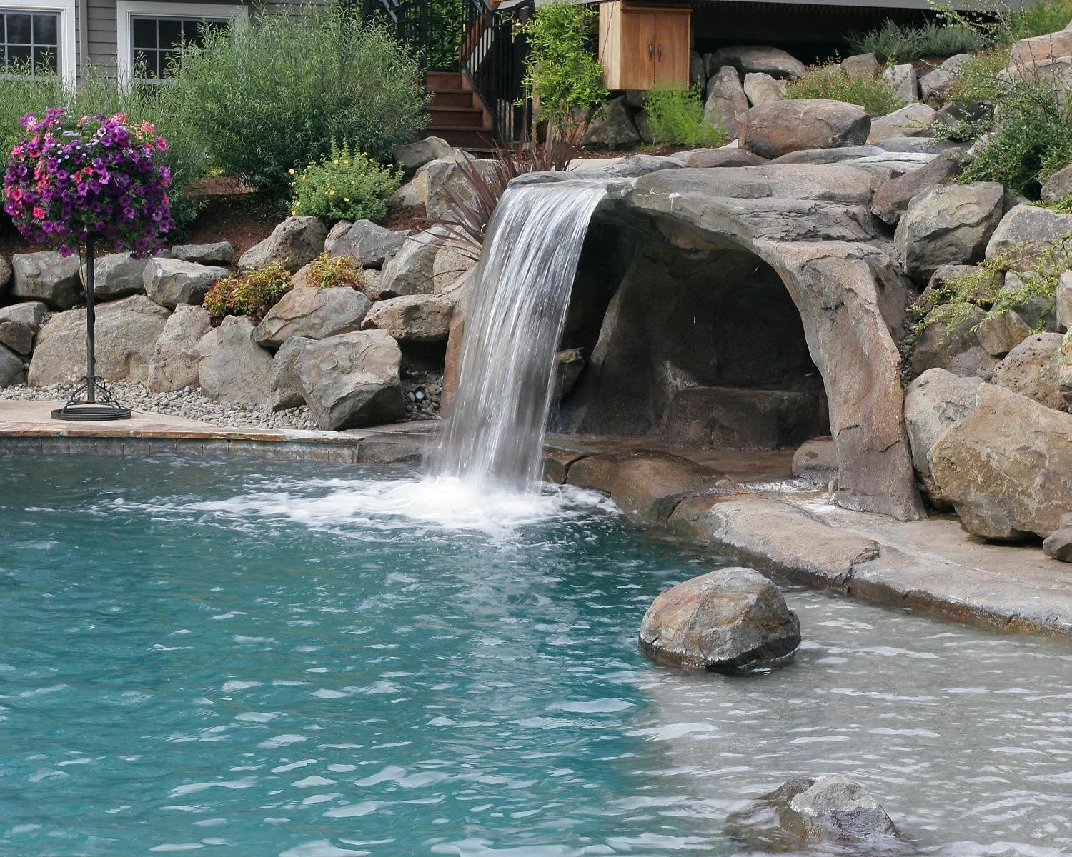 Inground pool with stone wall, plantings, and waterfall