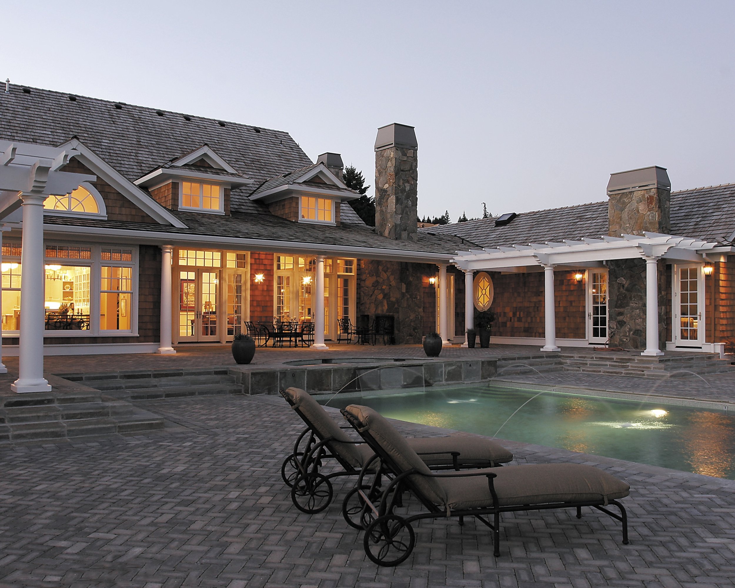 Inground pool with beautiful paver patio and white pergola at dusk
