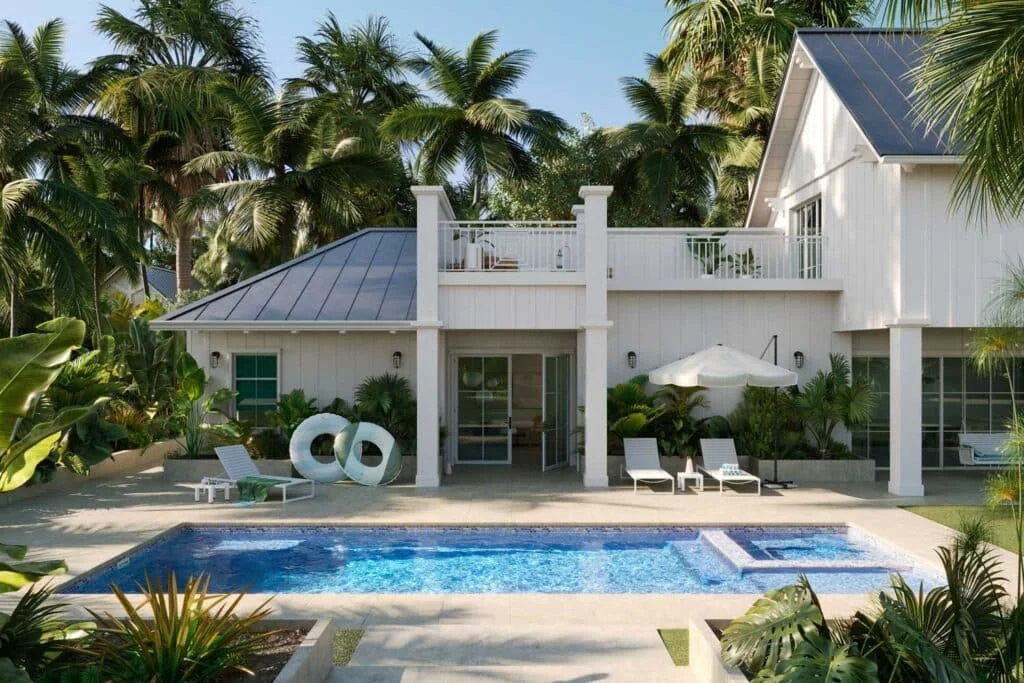 A white two-story house with a metal roof, surrounded by lush tropical plants and palm trees, featuring a backyard with a swimming pool and lounge chairs, under a clear blue sky.