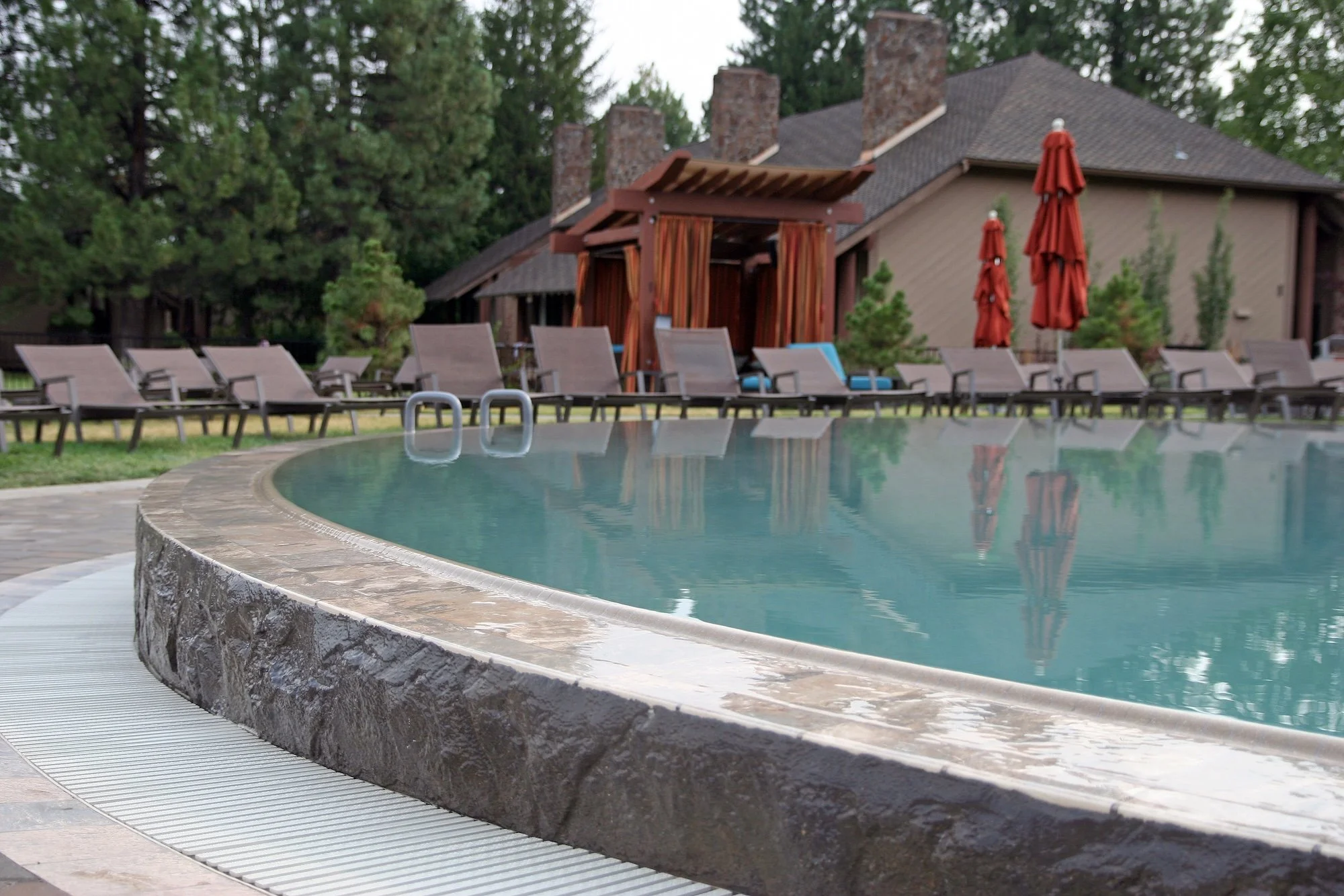 A swimming pool with a stone edge, surrounded by lounging chairs and patio umbrellas