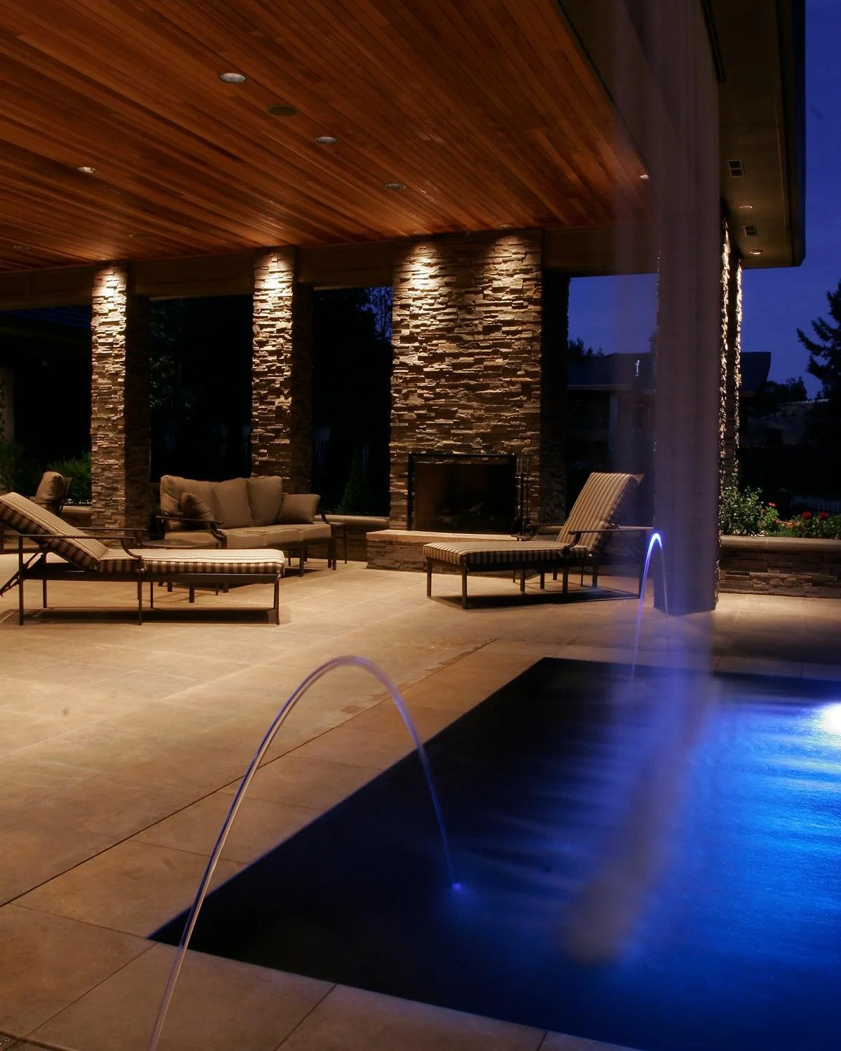 Inground pool at night with pool light and water fountains