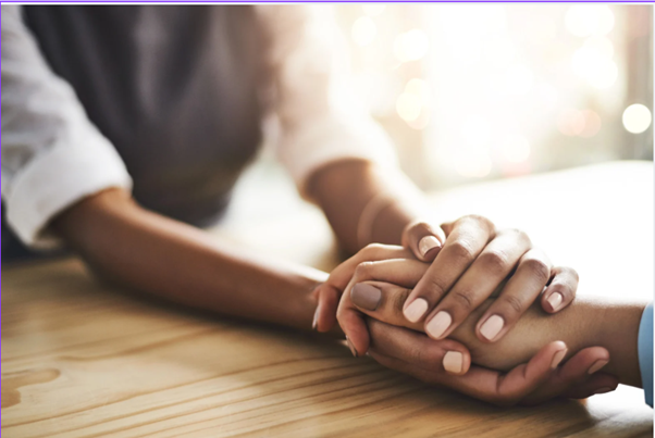 Two people holding hands on a wooden table, with sunlight in the background.